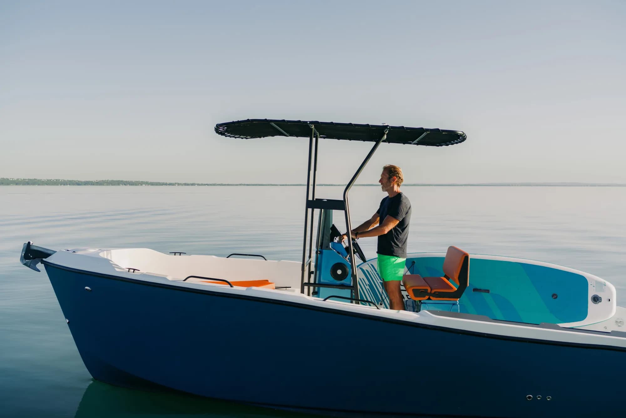 The blue-hulled Wia 230 CC under way, its open deck with orange cushions around the centre console under a black T-top.
