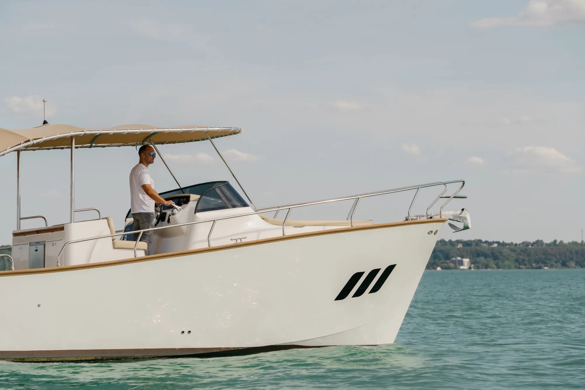 The white-hulled Wia 330 under way, its cream canvas top raised over the open cockpit and tan upholstery, with teak deck trim.