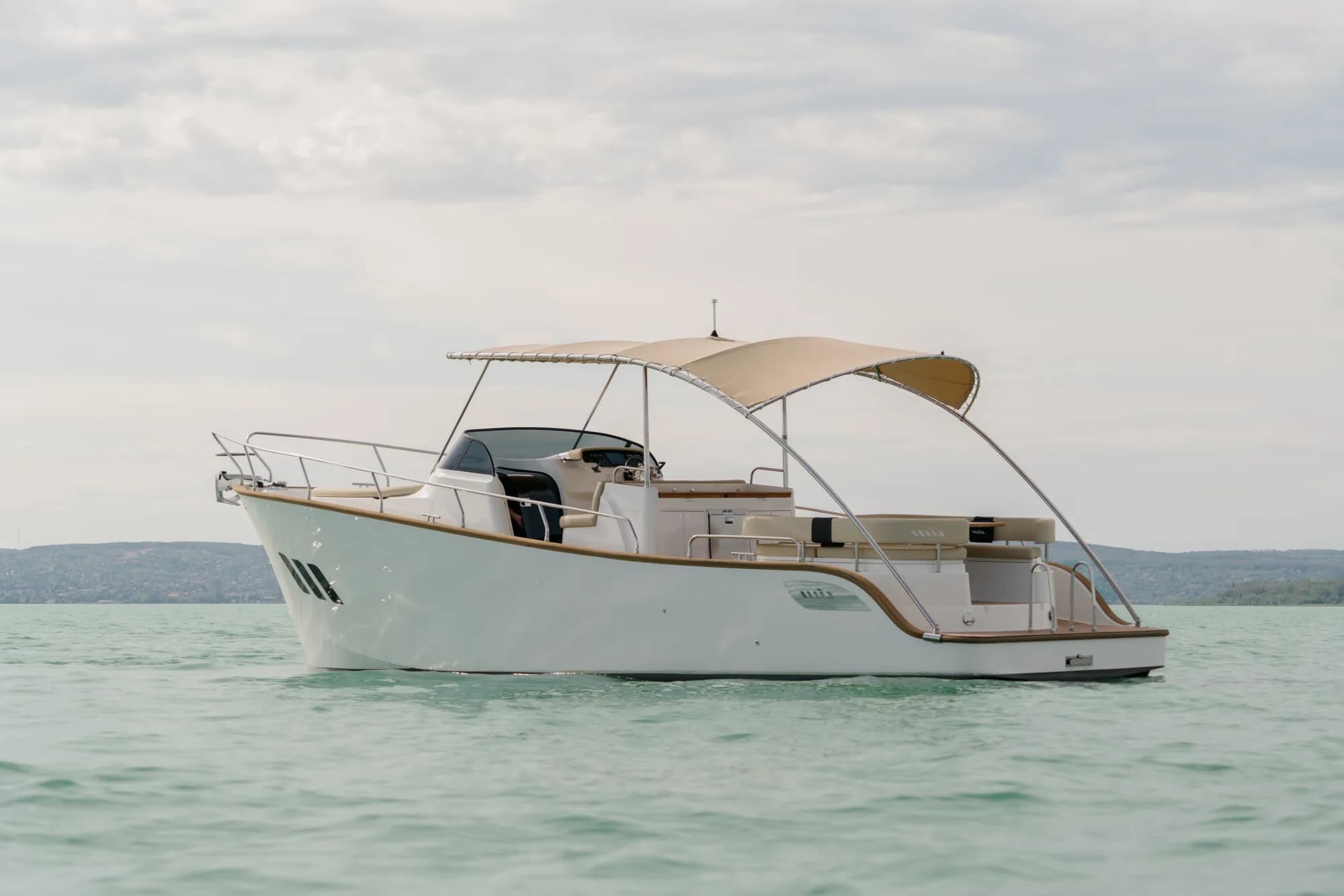 The white-hulled Wia 330 under way, its cream canvas top raised over the open cockpit and tan upholstery, with teak deck trim.