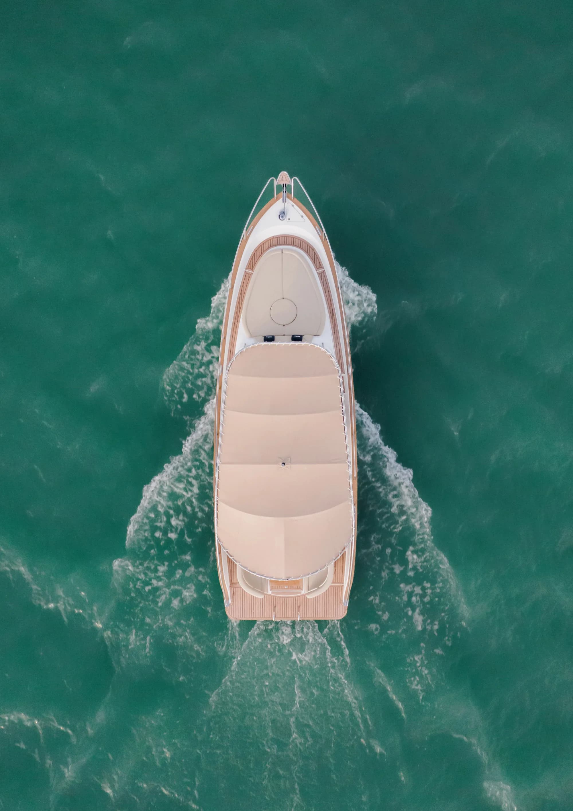 The Wia 330 seen from directly above on green water, its cream top, teak decks and tan cockpit seating laid out.