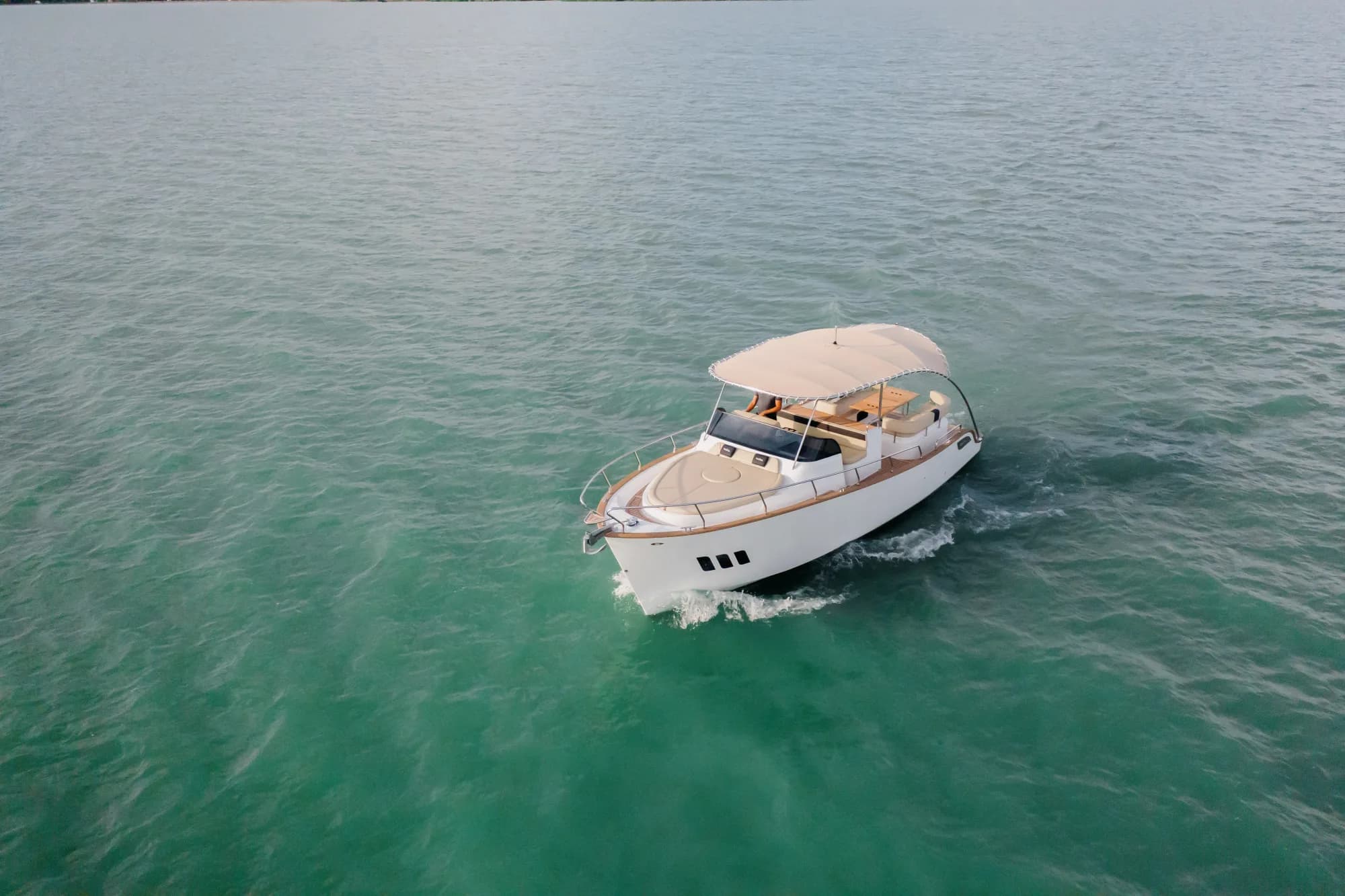 The white-hulled Wia 330 open dayboat with its cream canvas top under way on turquoise water, seen from the air.