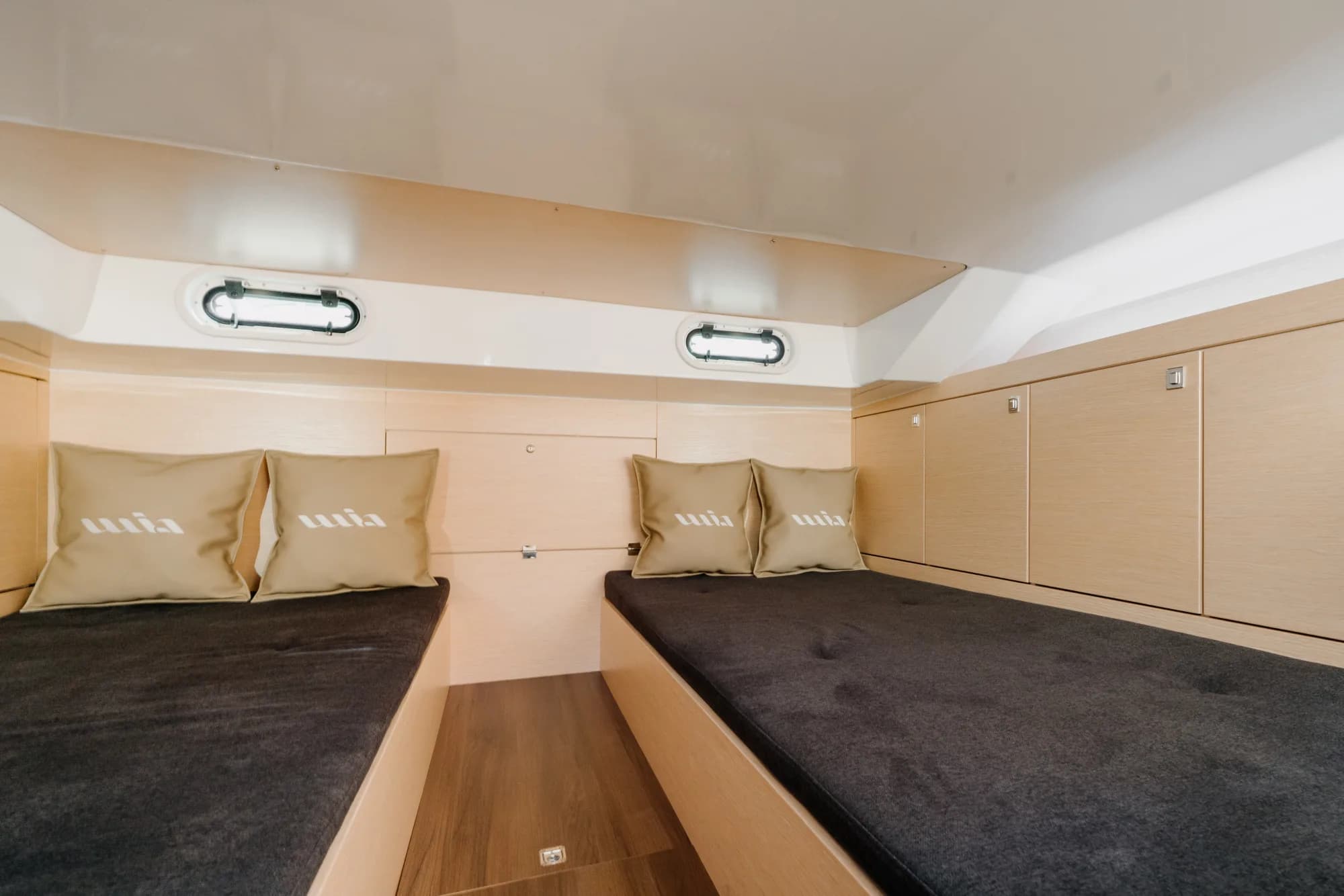 The below-deck cabin of the Wia 330: a U-shaped charcoal dinette around a light oak table, pale oak panelling, a round overhead hatch and nautical anchor-print cushions.