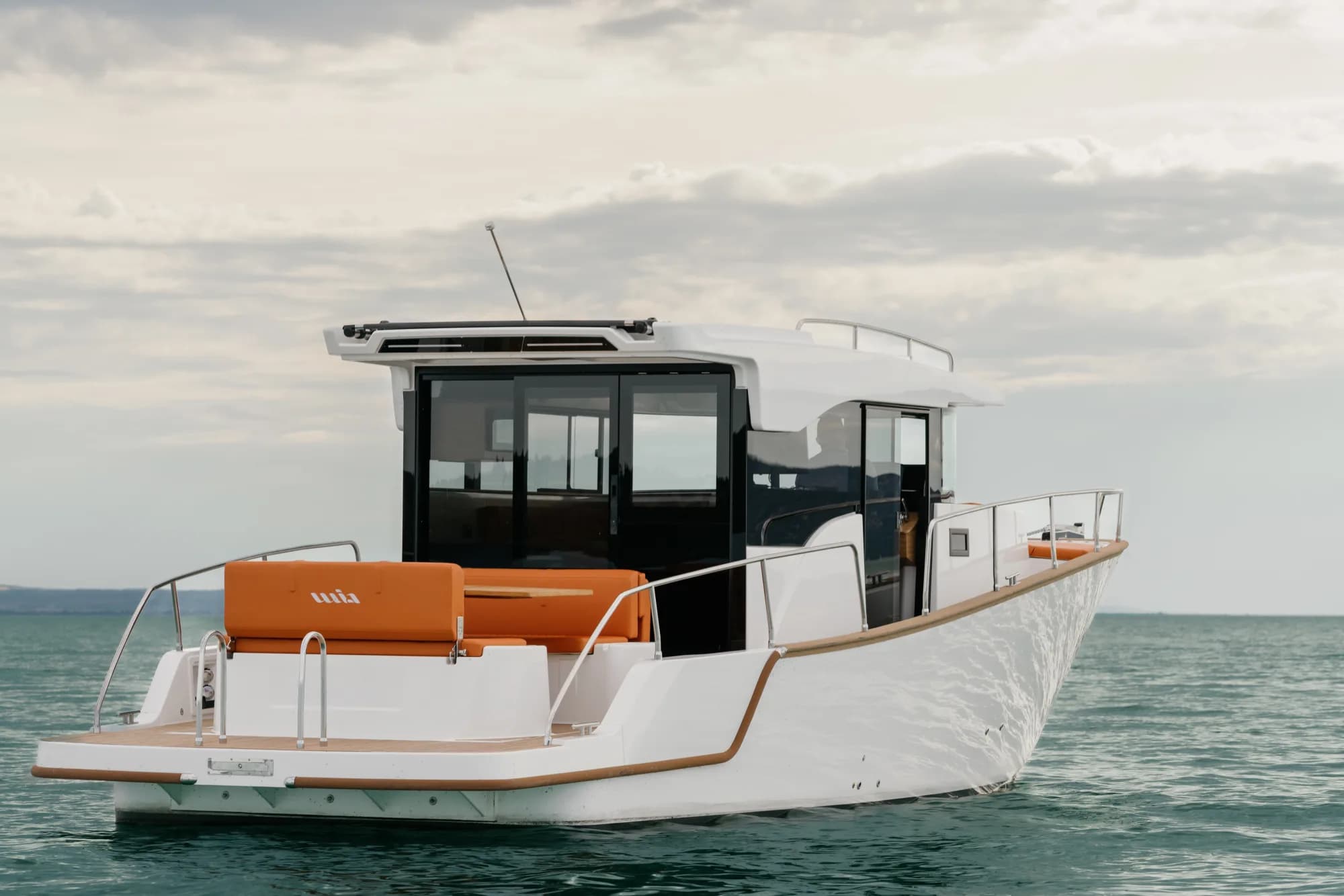 The white-hulled Wia 350 under way, its white hardtop over the enclosed helm and orange cushions in the cockpit.