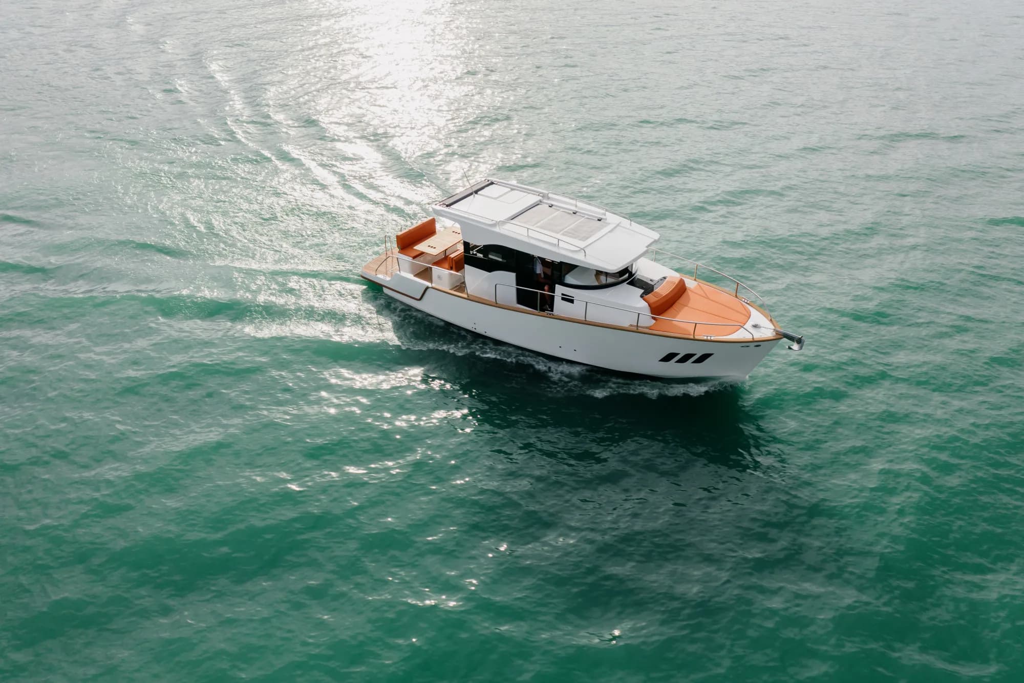 The white-hulled Wia 350 under way, its white hardtop over the enclosed helm and orange cushions in the cockpit.