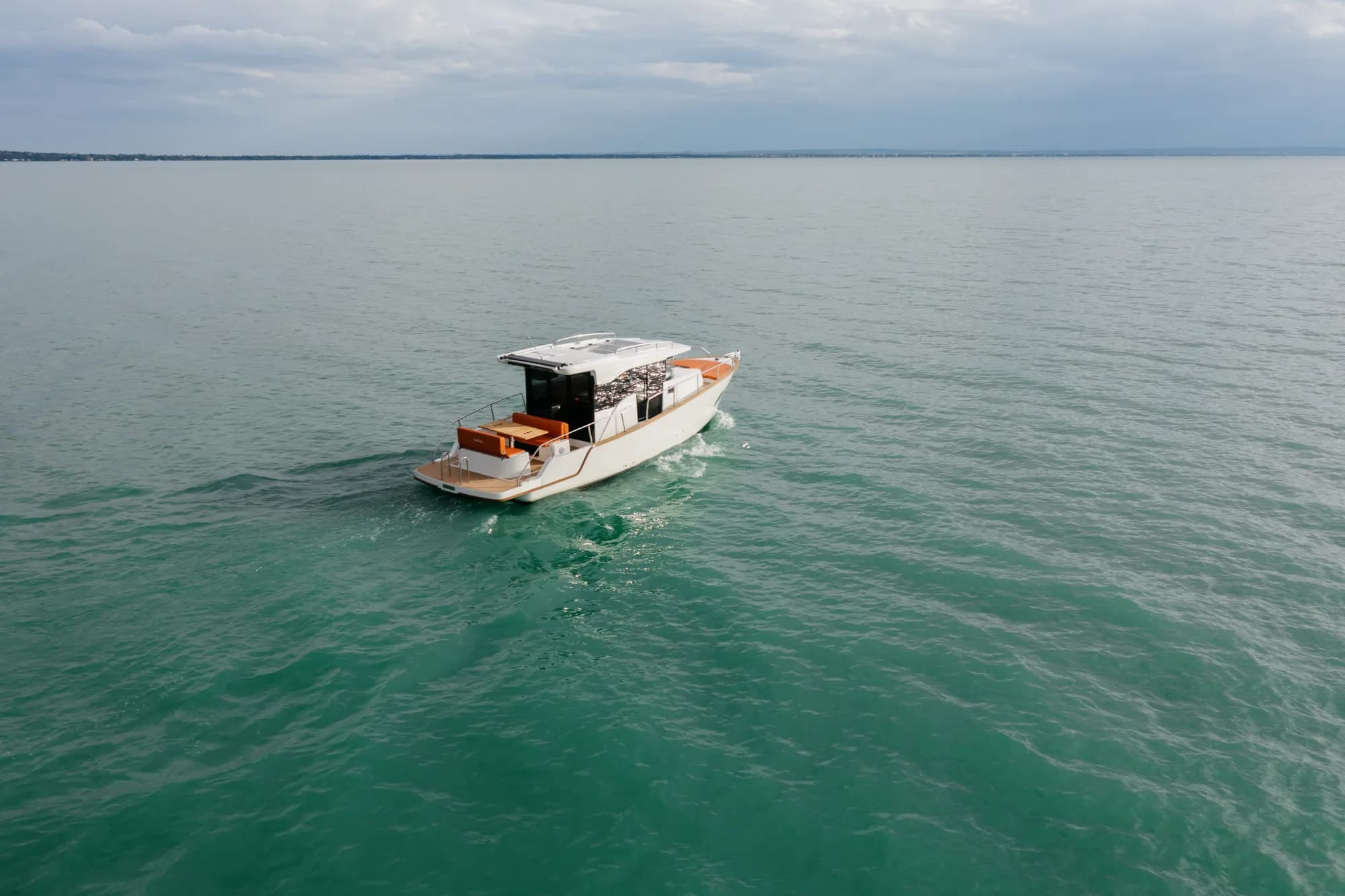 The white-hulled Wia 350 under way, its white hardtop over the enclosed helm and orange cushions in the cockpit.
