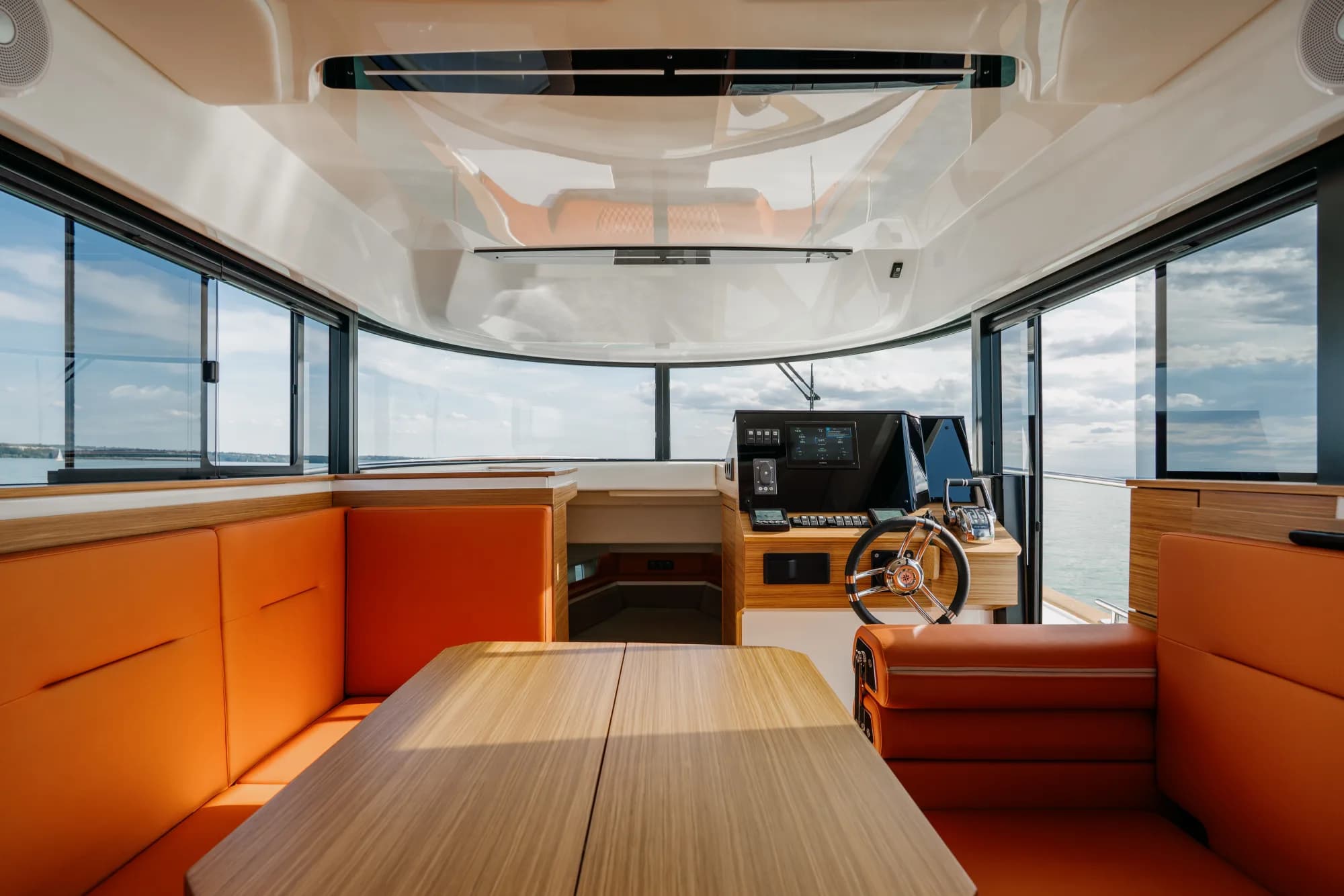 The enclosed wheelhouse of the Wia 350: bright orange leather seating, a light oak dinette, a chrome-spoked helm and a touchscreen at the console, wrapped in panoramic windows.