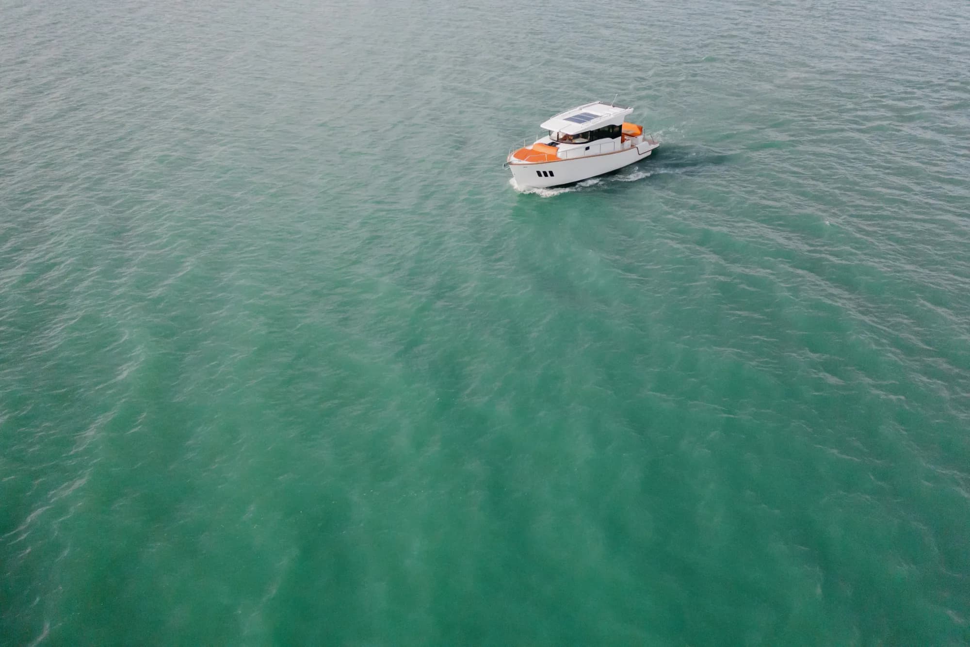 The Wia 350 seen from high above, a white hardtop cruiser cutting a wake across shimmering green water.