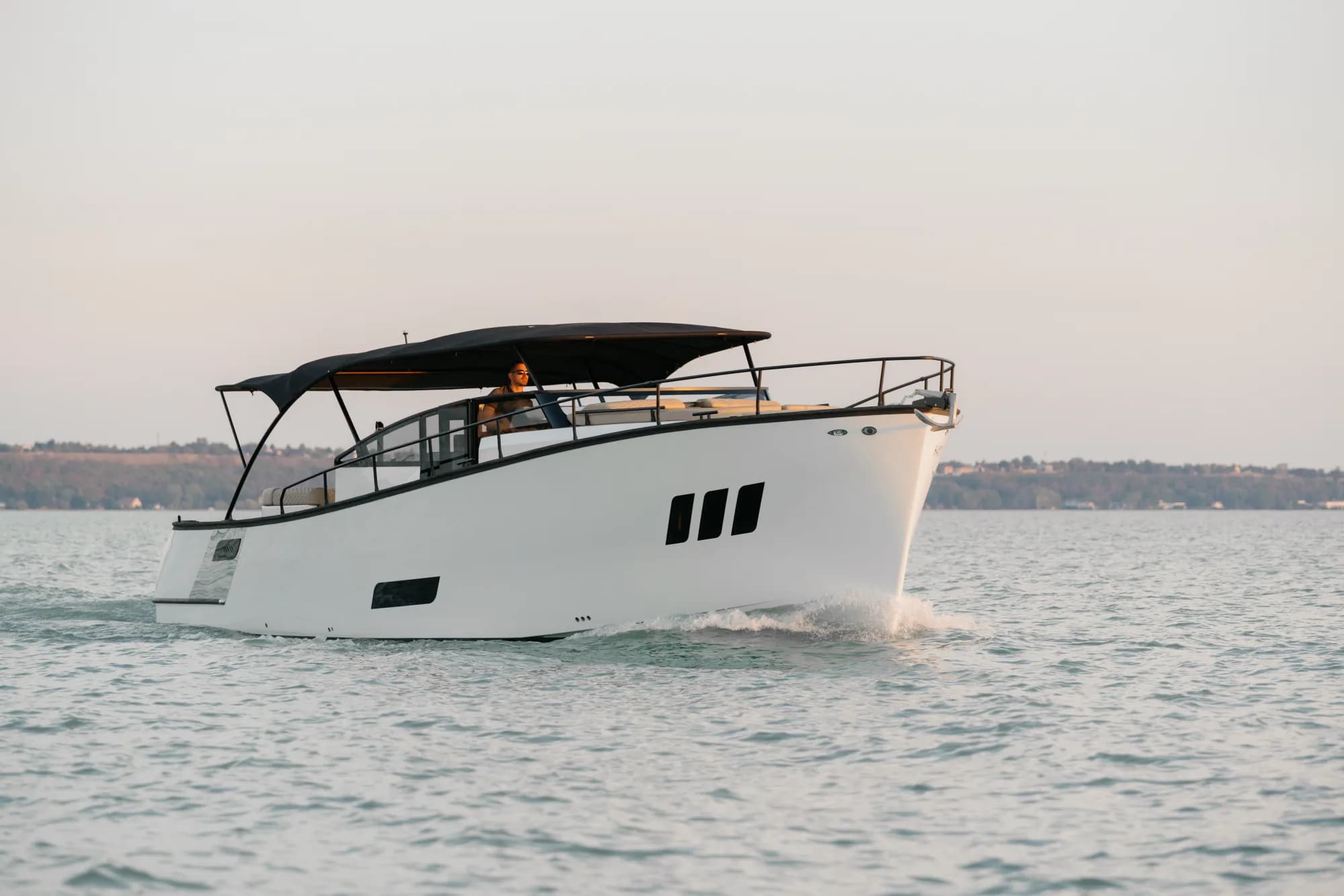 The white-hulled Wia 450 Cabrio under way on the water at dusk, its black canvas top raised over the open cockpit.