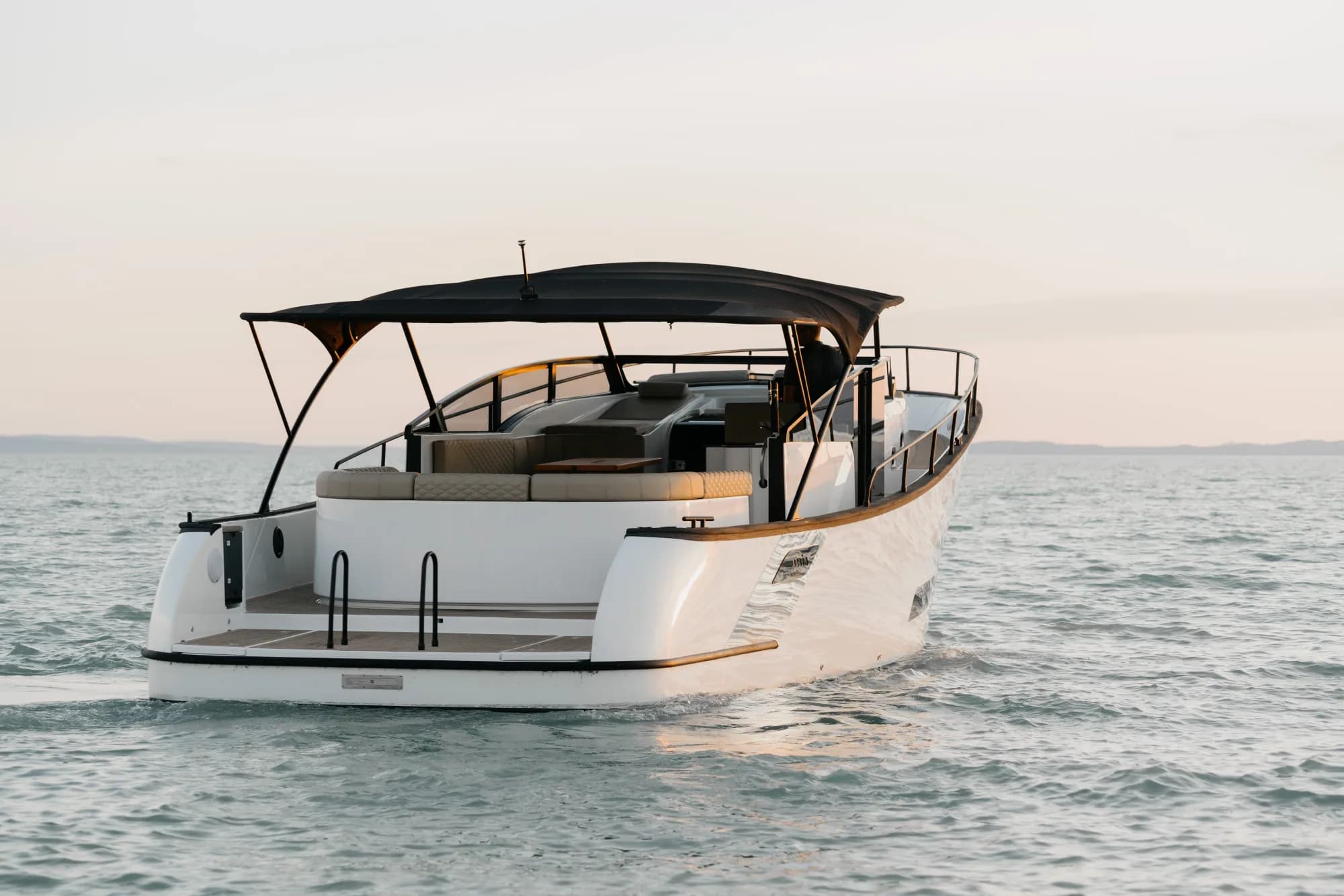 The white-hulled Wia 450 Cabrio under way on the water at dusk, its black canvas top raised over the open cockpit.