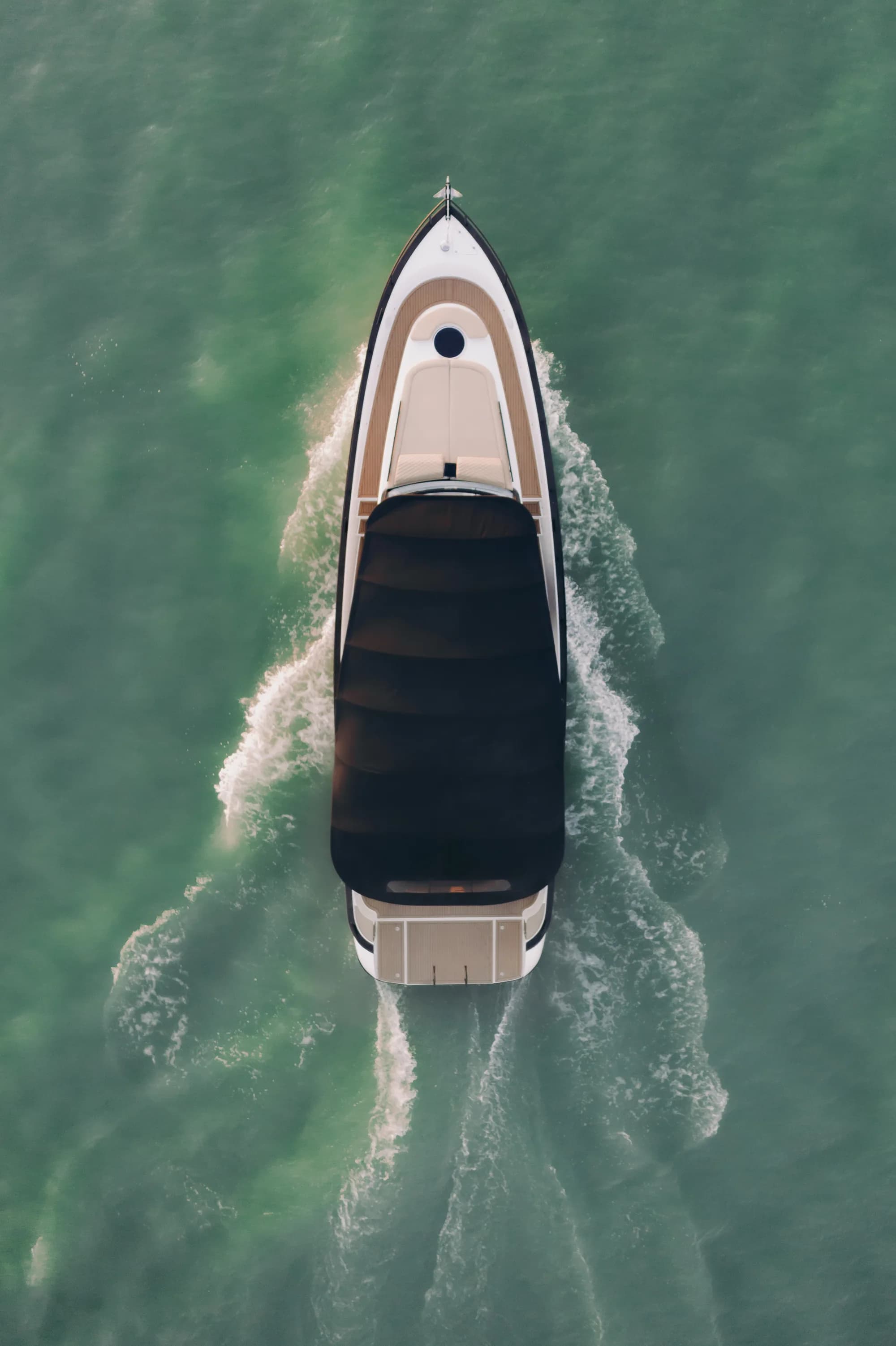 The Wia 450 Cabrio seen from directly above on green water, its open cockpit and cream sunpads laid out under the retracted top.