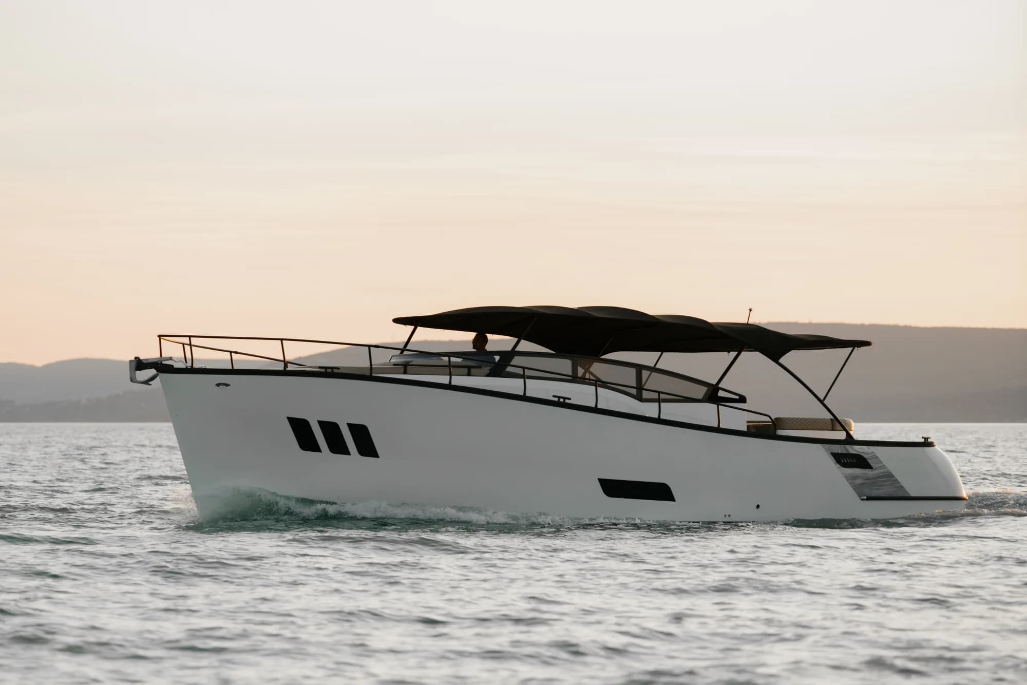 The white-hulled Wia 450 Cabrio with its black canvas top under way on Lake Balaton at dusk, seen from the air.