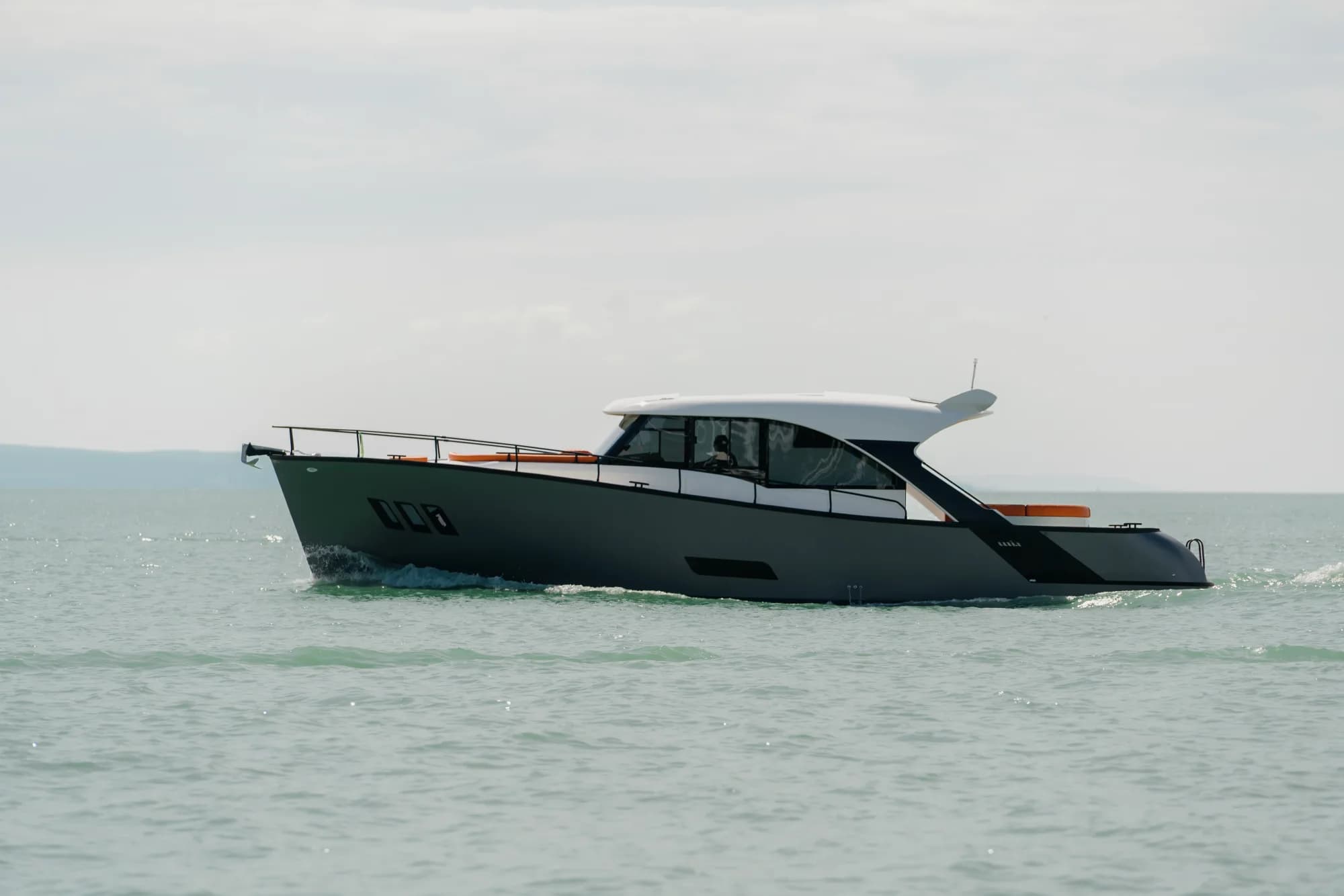 The dark-grey-hulled Wia 450 HardTop under way, its white hardtop over the enclosed helm and orange sunpads on the foredeck.