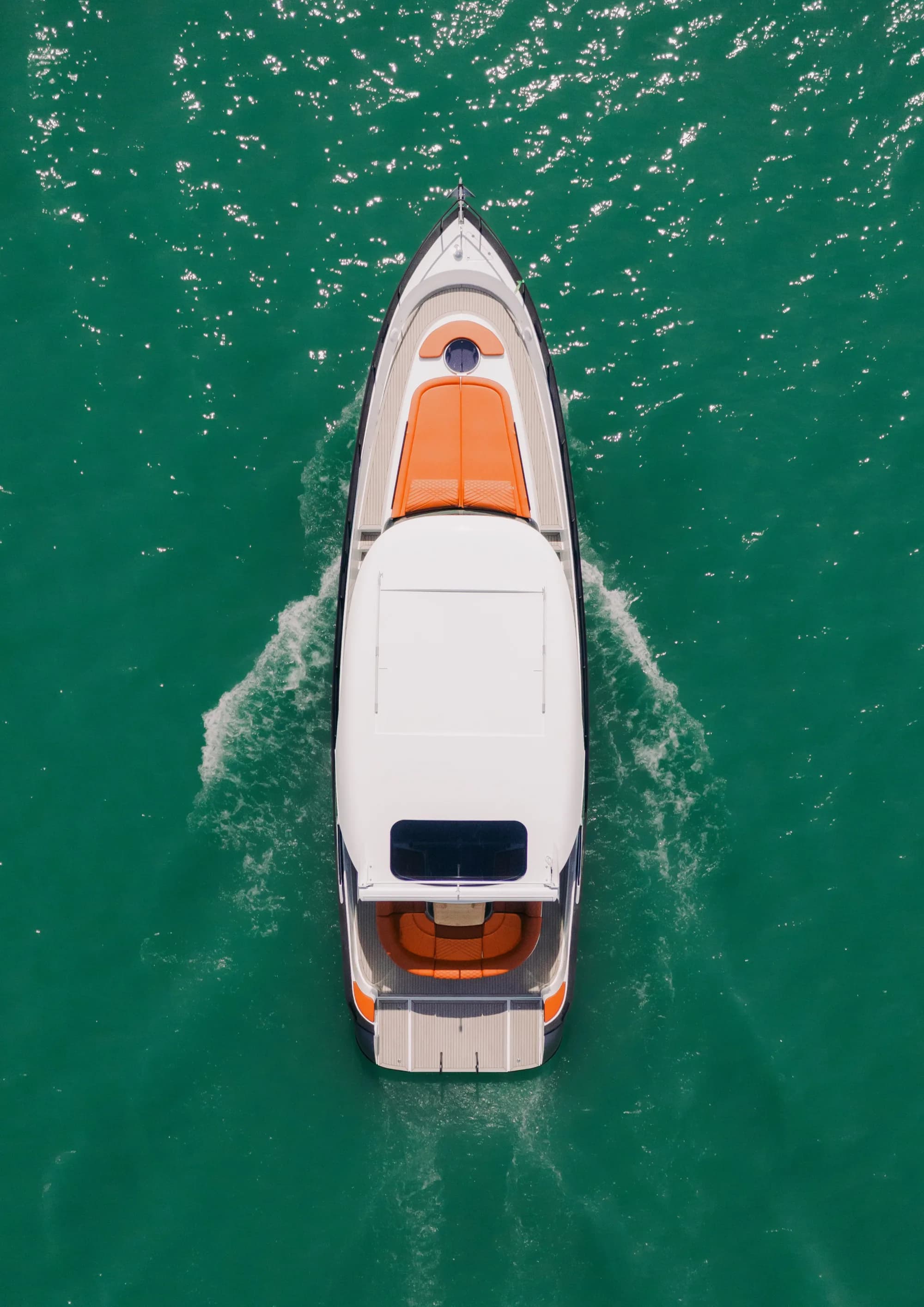 The Wia 450 HardTop seen from directly above, its white hardtop, teak side decks and orange foredeck sunpads on green water.