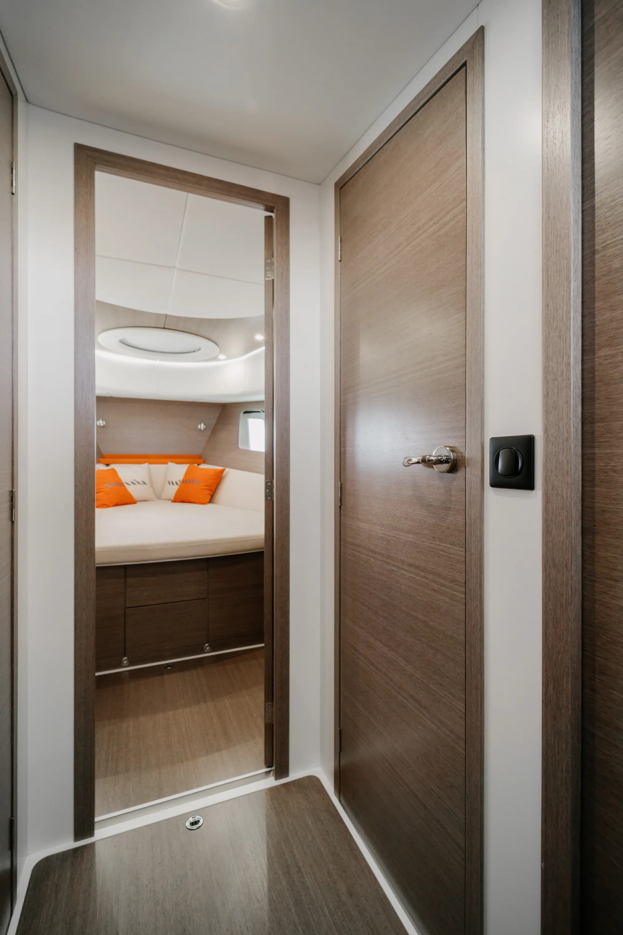 The enclosed saloon of the Wia 450 HardTop: orange leather seating with wia cushions, a light oak dinette, a galley with a dark worktop and the helm ahead, wrapped in panoramic windows.