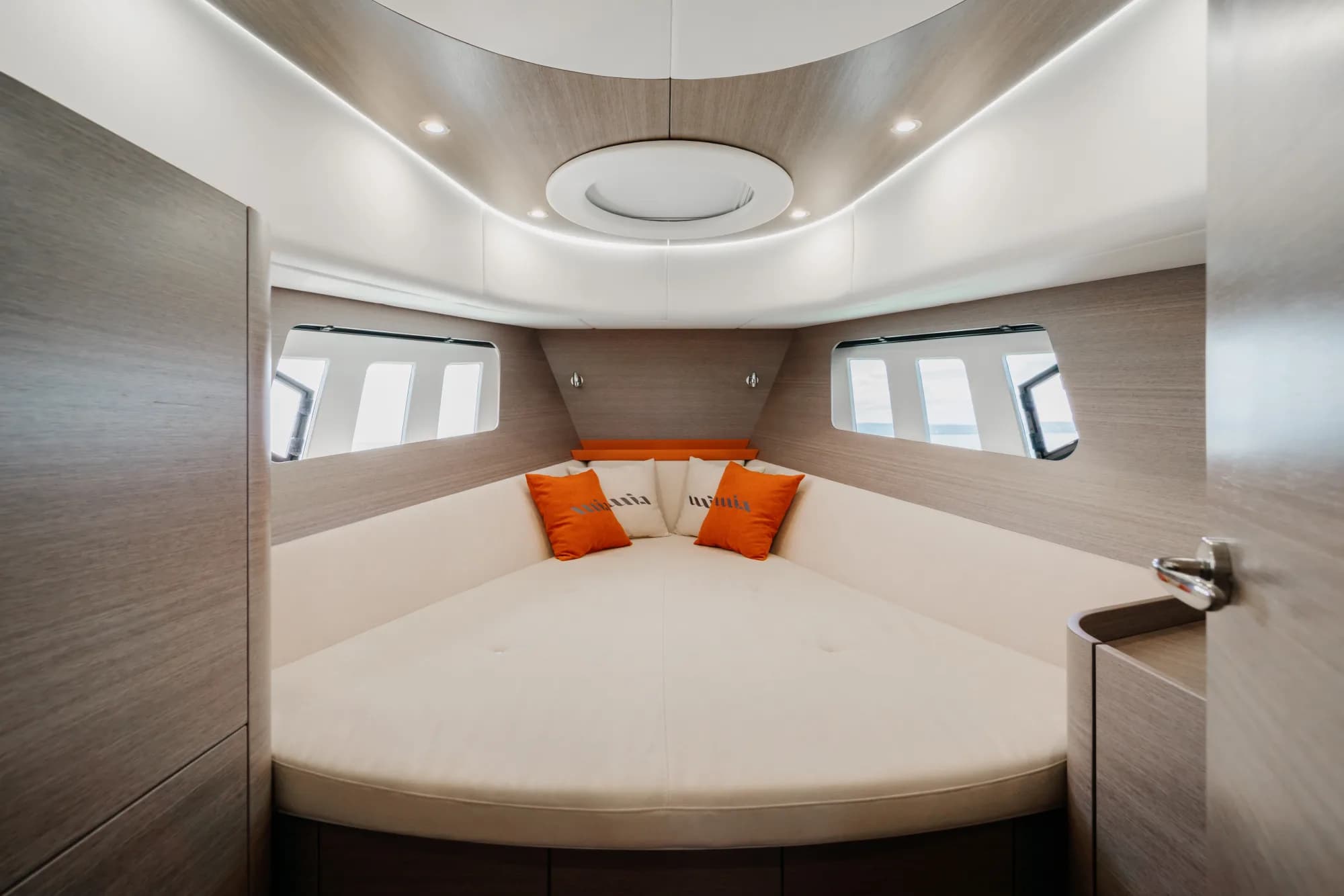 The enclosed saloon of the Wia 450 HardTop: orange leather seating with wia cushions, a light oak dinette, a galley with a dark worktop and the helm ahead, wrapped in panoramic windows.