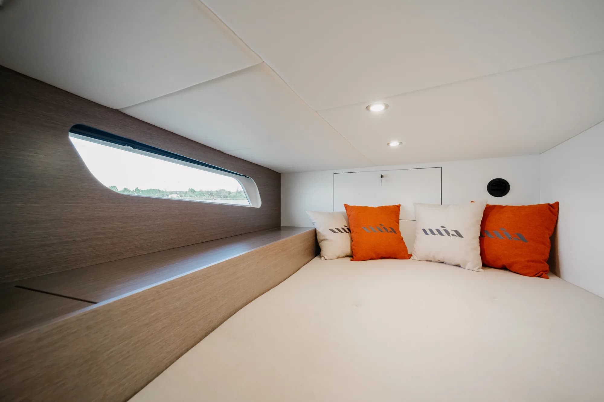 The enclosed saloon of the Wia 450 HardTop: orange leather seating with wia cushions, a light oak dinette, a galley with a dark worktop and the helm ahead, wrapped in panoramic windows.