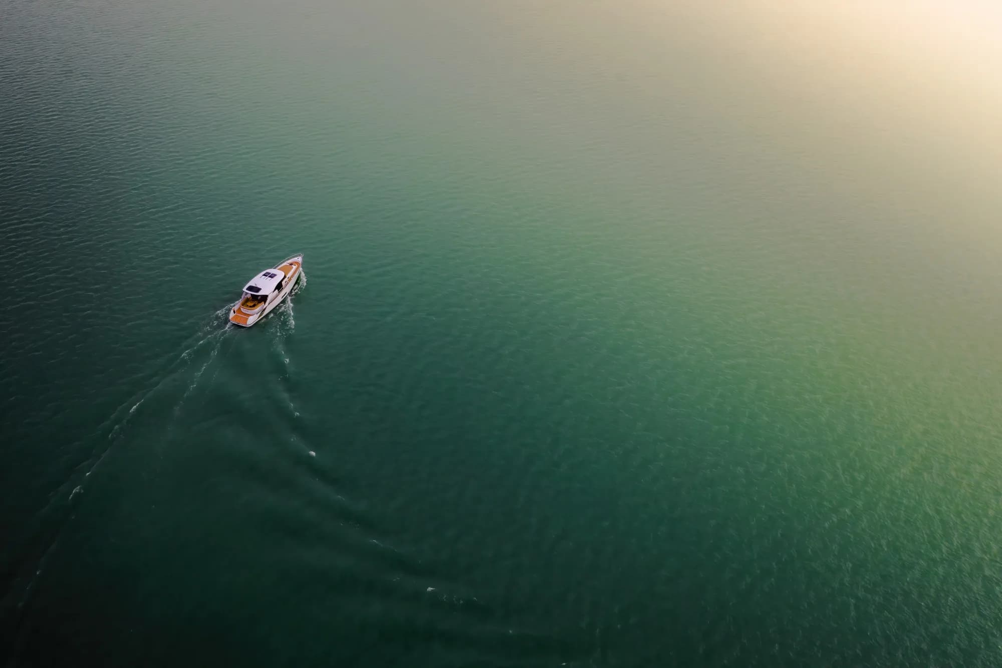 The Wia 450 HardTop seen from high above, a dark-hulled cruiser with a white hardtop cutting a wake across shimmering green water.