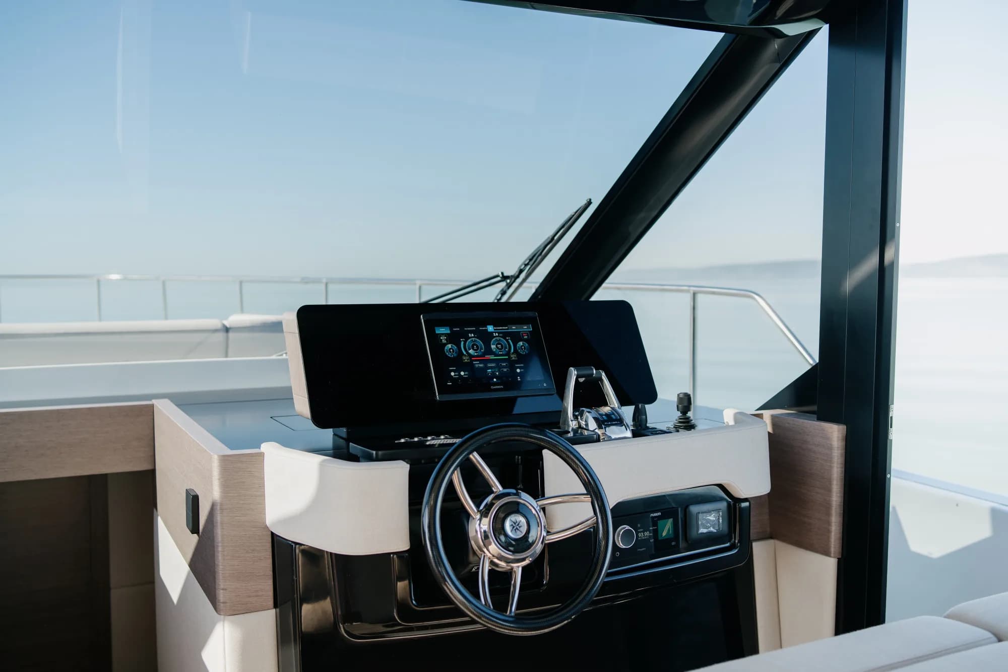 The enclosed saloon of the Wia 520 HardTop: a cream L-shaped sofa, light oak panelling, a galley with a dark worktop, a teak sole and the helm ahead, wrapped in panoramic windows.