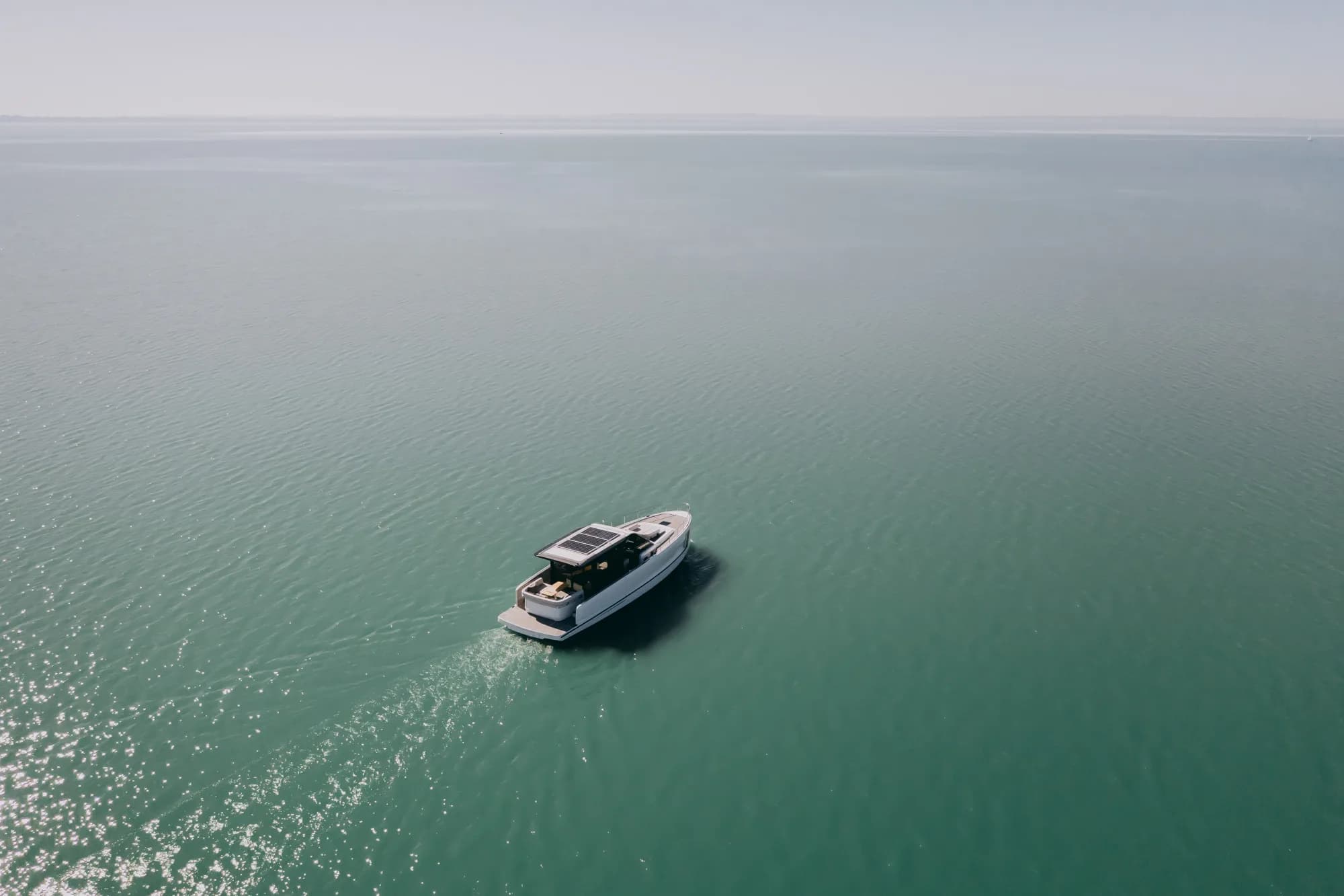 The Wia 520 HardTop seen from high above, a white cruiser with a dark hardtop leaving a wake across backlit green water.