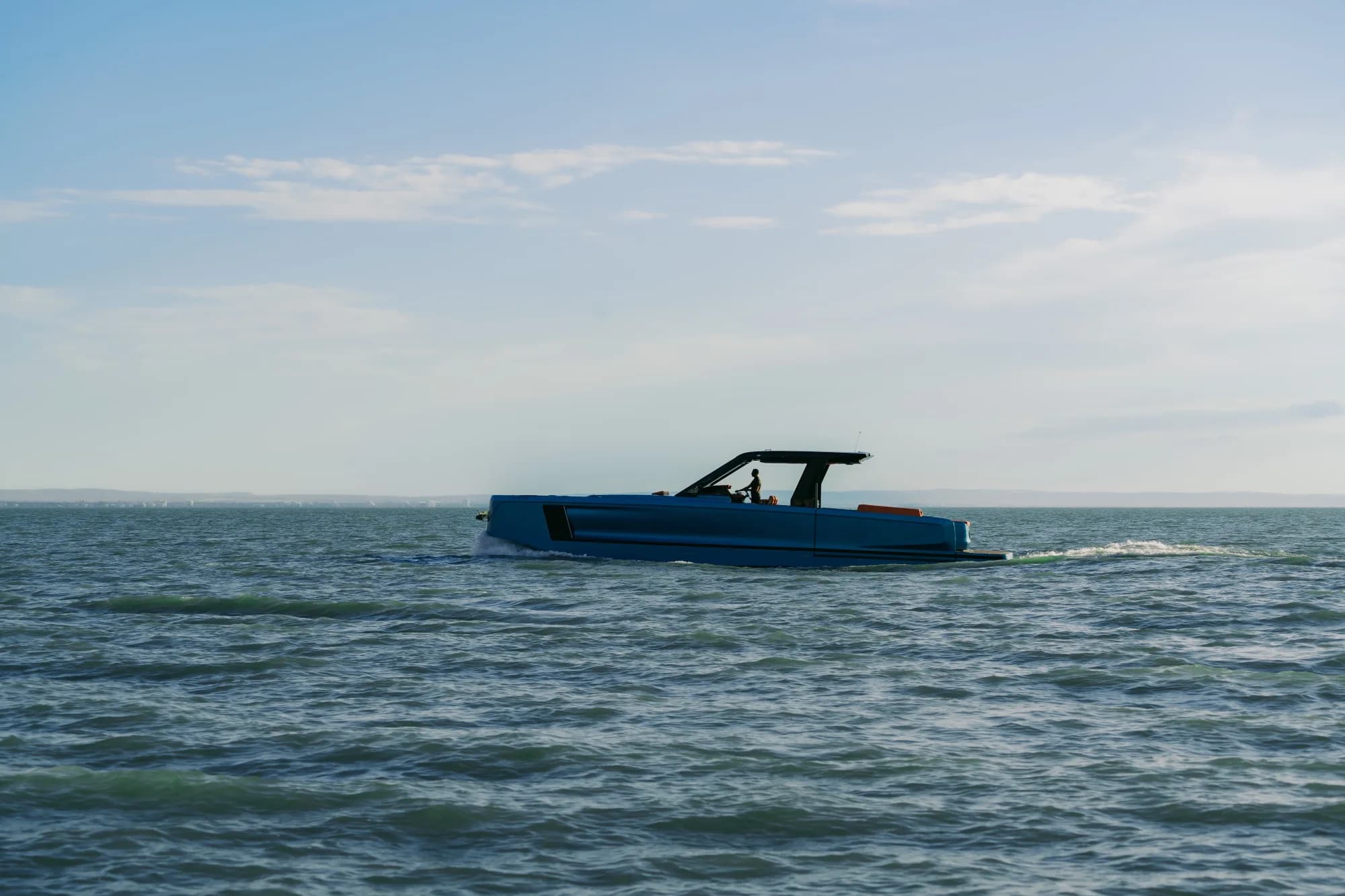 The blue-hulled Wia 520 Open under way on turquoise water, its orange cockpit and solar hardtop catching the light.