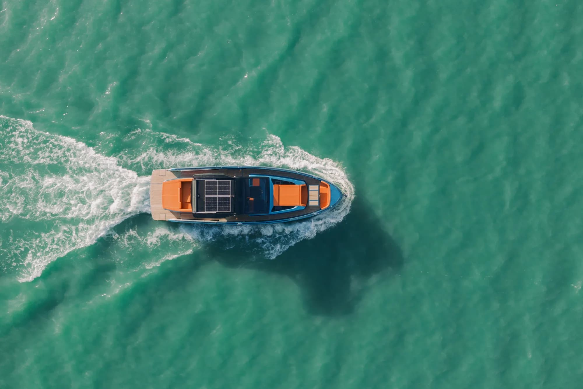 The blue-hulled Wia 520 Open cruising on open water, its orange cockpit and solar hardtop lit by the sun.