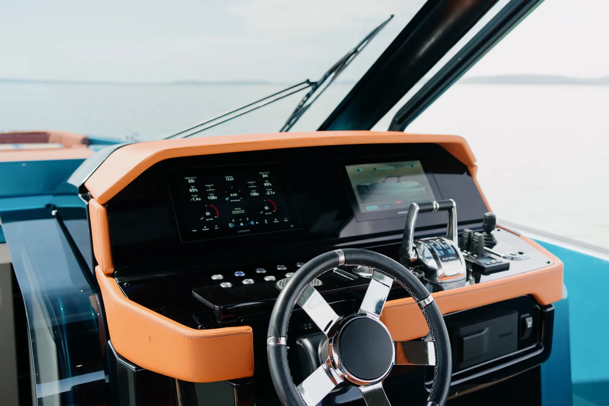 The helm of the Wia 520 Open: chrome wheel, switch panel and twin chartplotters set into the orange dashboard.