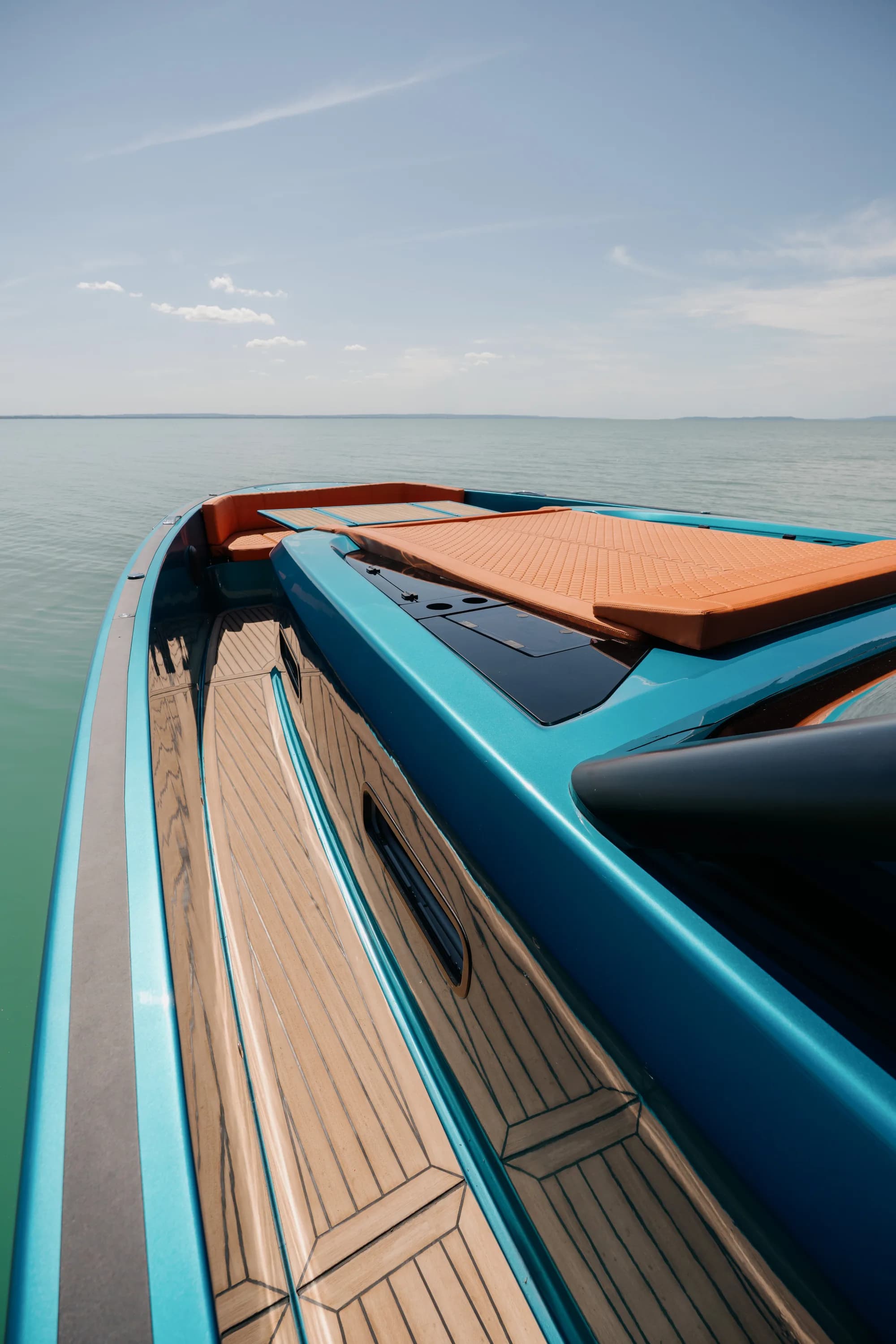 Detail of the Wia 520 Open: quilted orange leather cushions beside the pale teak deck and the blue hull edge.
