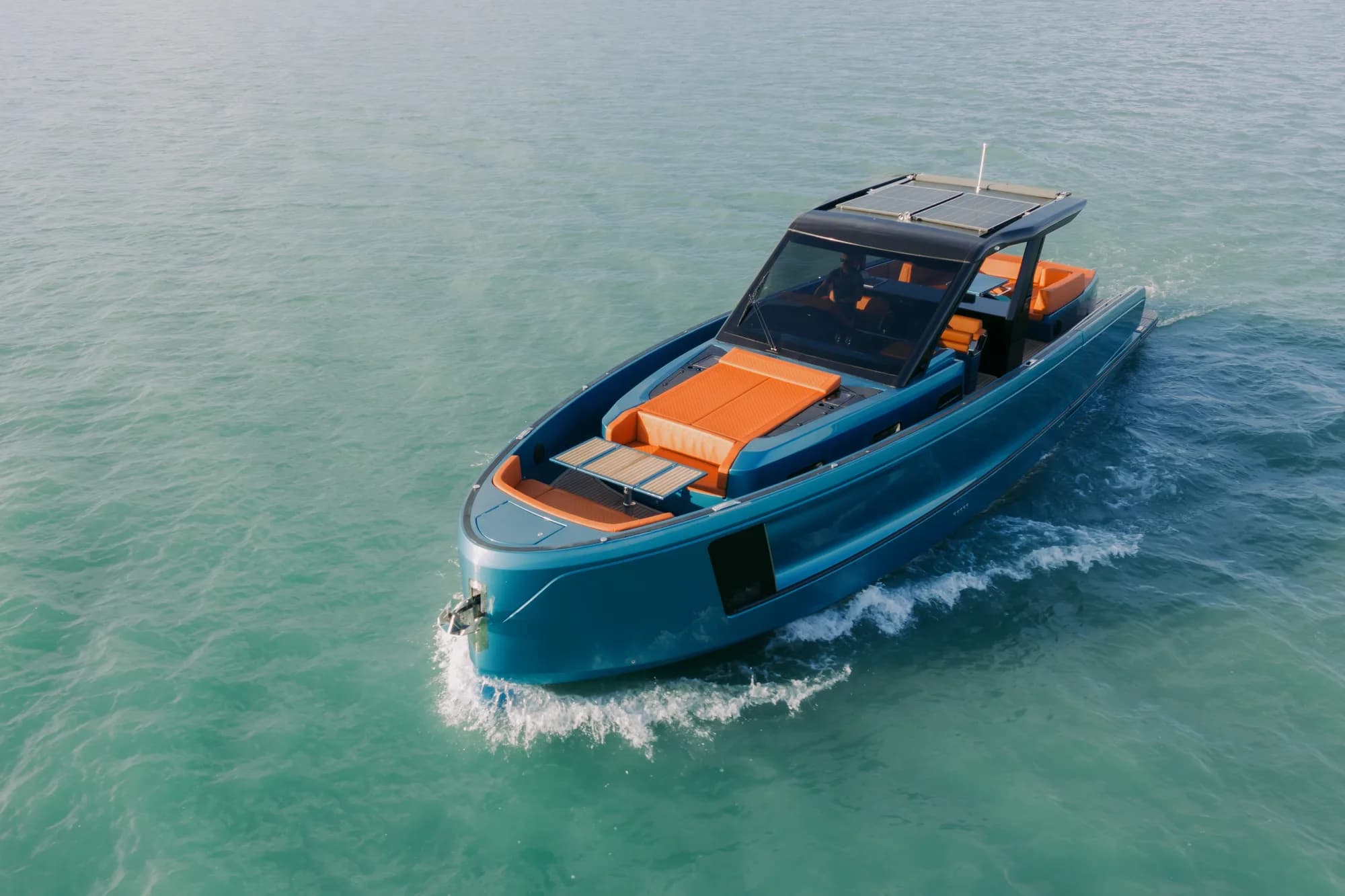 The blue-hulled Wia 520 Open with orange upholstery and a solar-panelled hardtop cruising on the turquoise water of Lake Balaton, seen from above.
