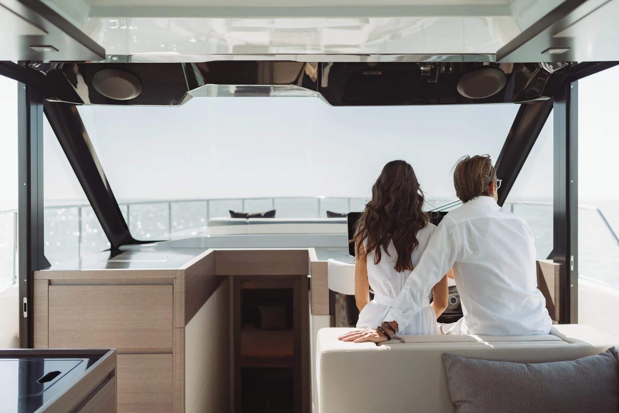 A couple sitting in the saloon of a Wia, looking out through the windscreen at the water.