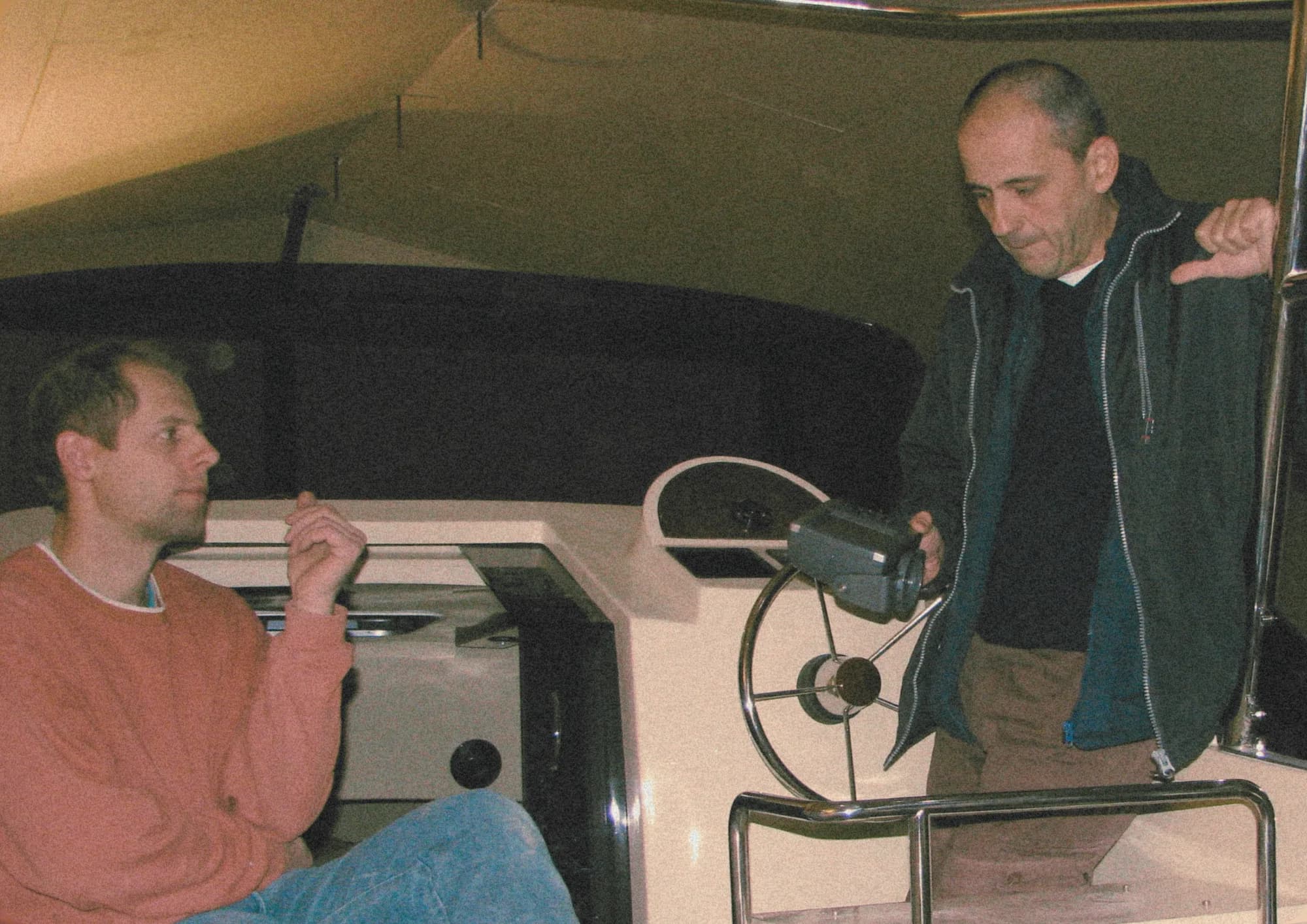 Two men in conversation at the helm of an early Wia, one seated and one standing, in a warm vintage tone.