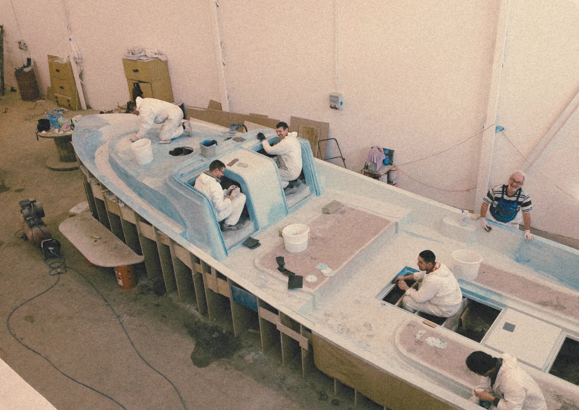 Overhead view of workers in white coveralls laminating a large Wia deck mould inside the workshop.