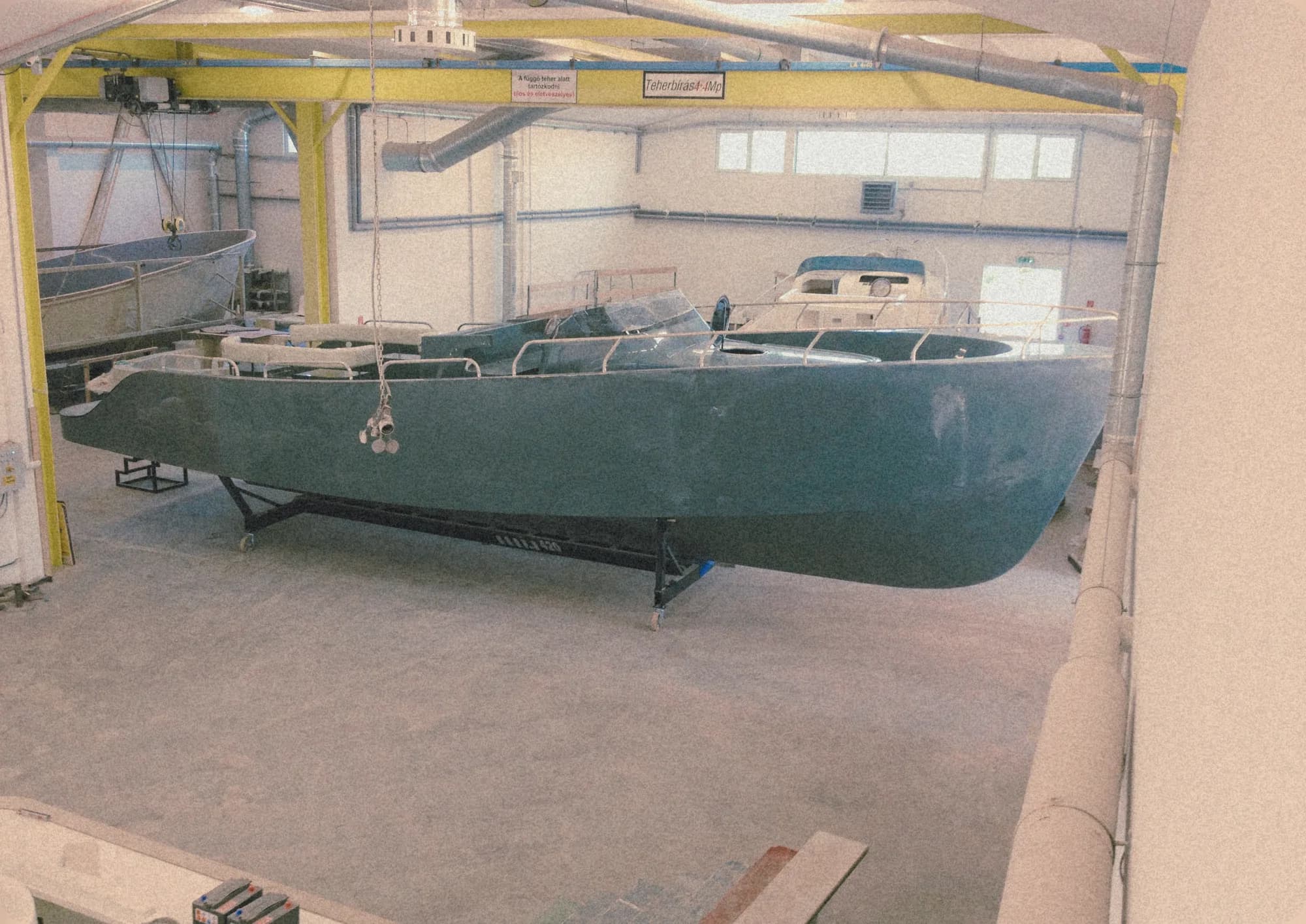 A dark green Wia hull under construction on a cradle inside the workshop, an overhead crane above.