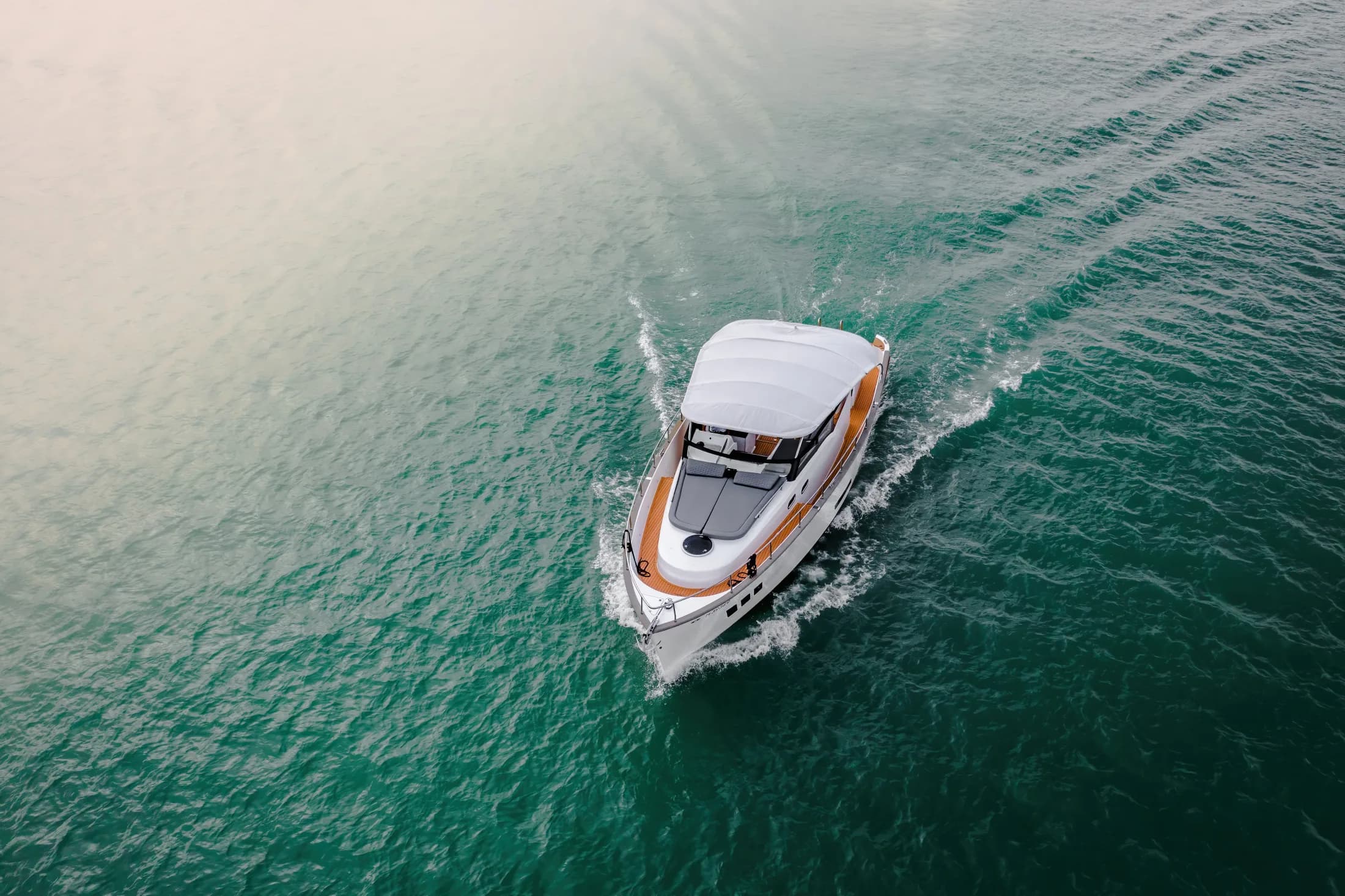 Vue aérienne d'un Wia blanc avec bimini blanc naviguant sur une eau turquoise, laissant un sillage.