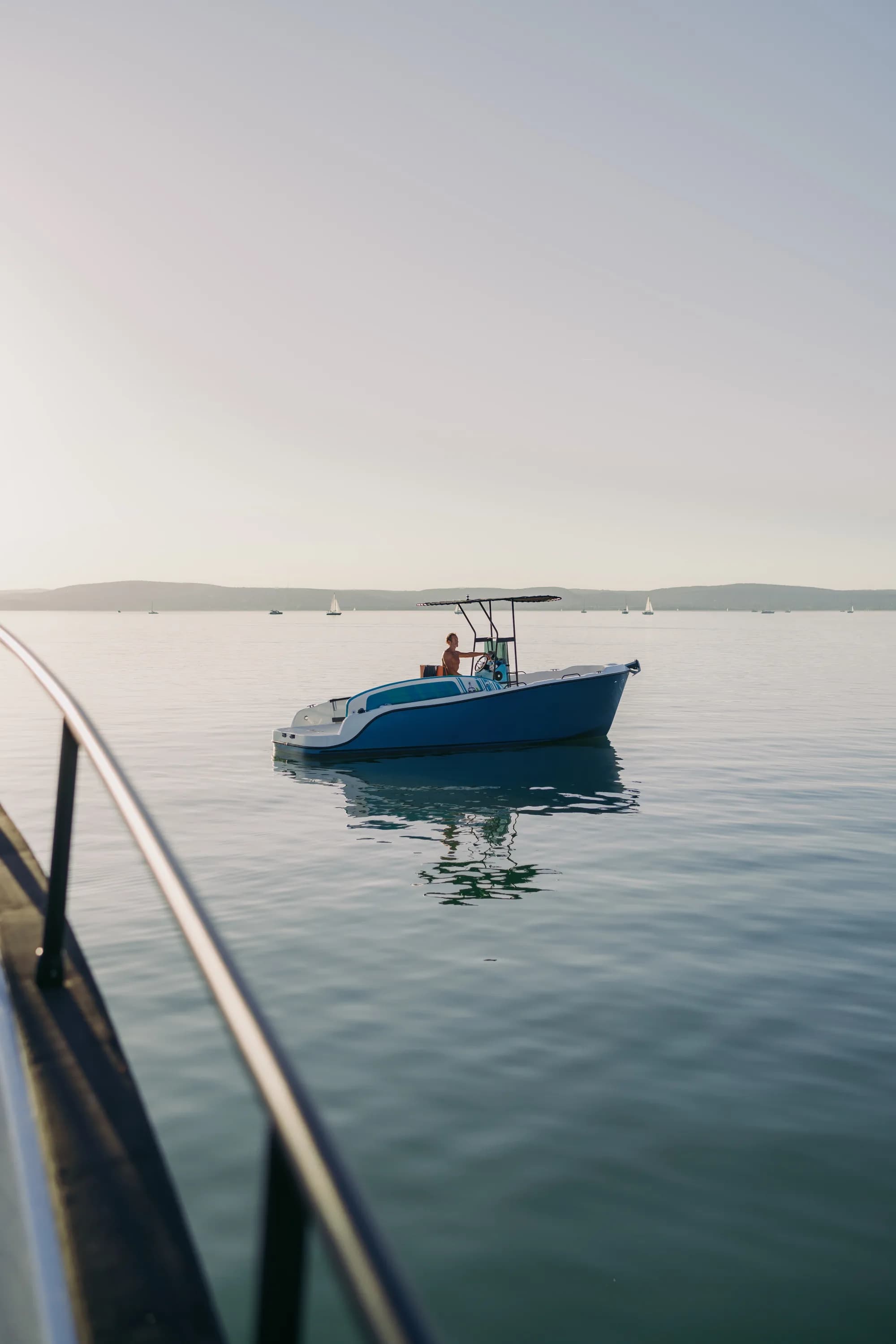 The blue-hulled Wia 230 CC under way, its open deck with orange cushions around the centre console under a black T-top.