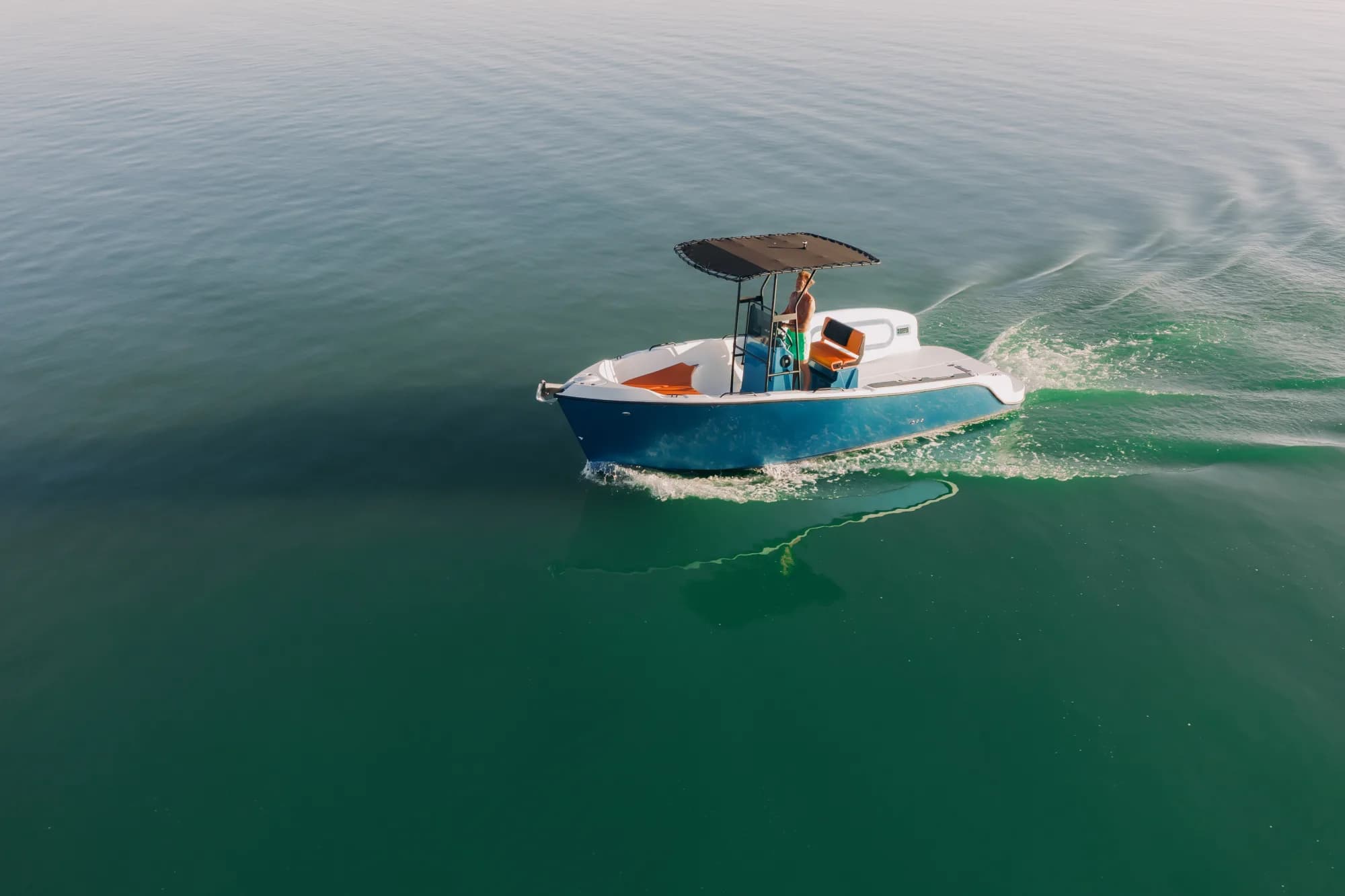 The blue-hulled Wia 230 CC under way, its open deck with orange cushions around the centre console under a black T-top.