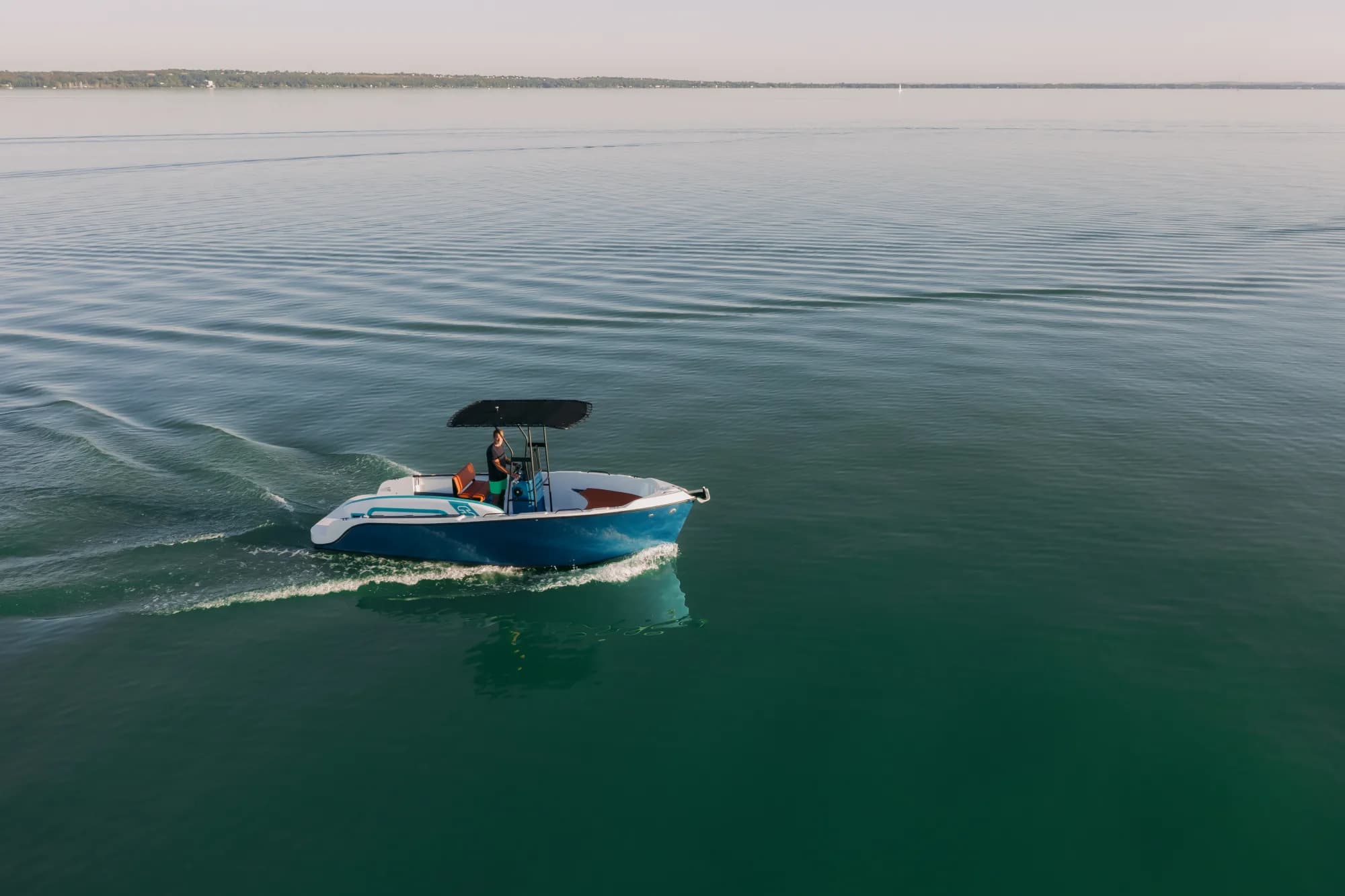 The blue-hulled Wia 230 CC under way, its open deck with orange cushions around the centre console under a black T-top.