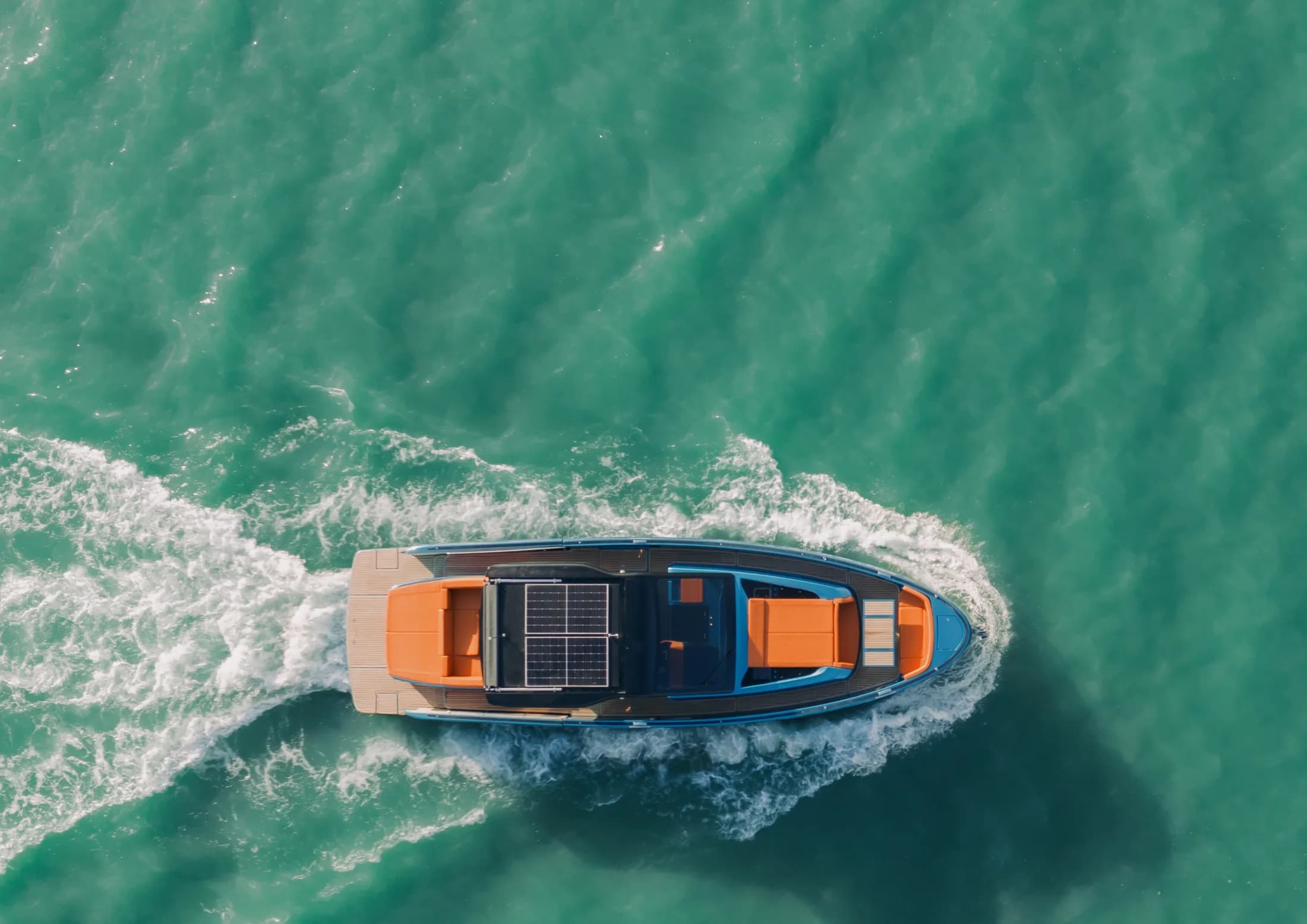 Overhead aerial of a Wia with orange leather seating and deck solar panels cruising through turquoise water.