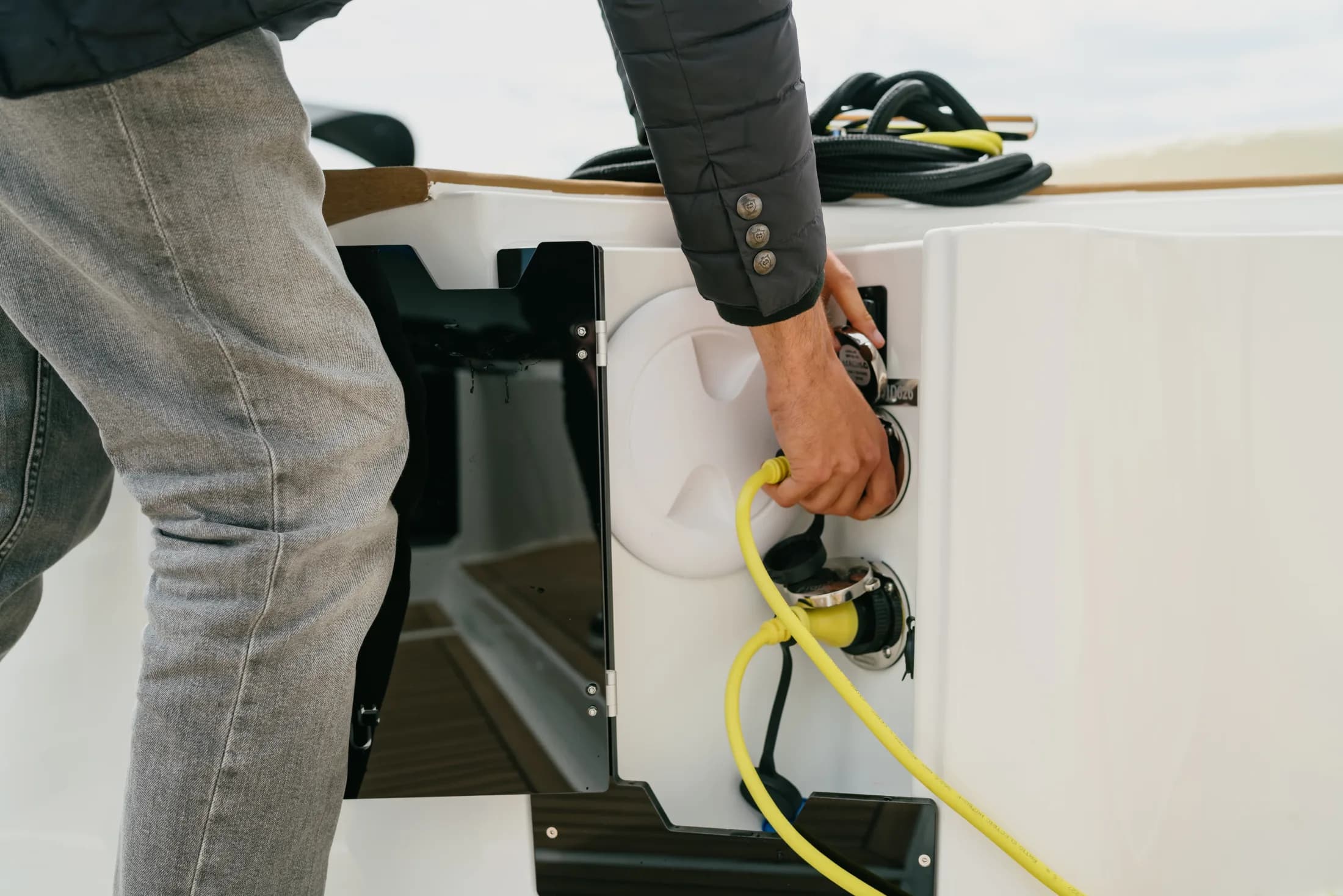 A hand plugging a yellow shore-power cable into the charging inlet on the white hull of a Wia.