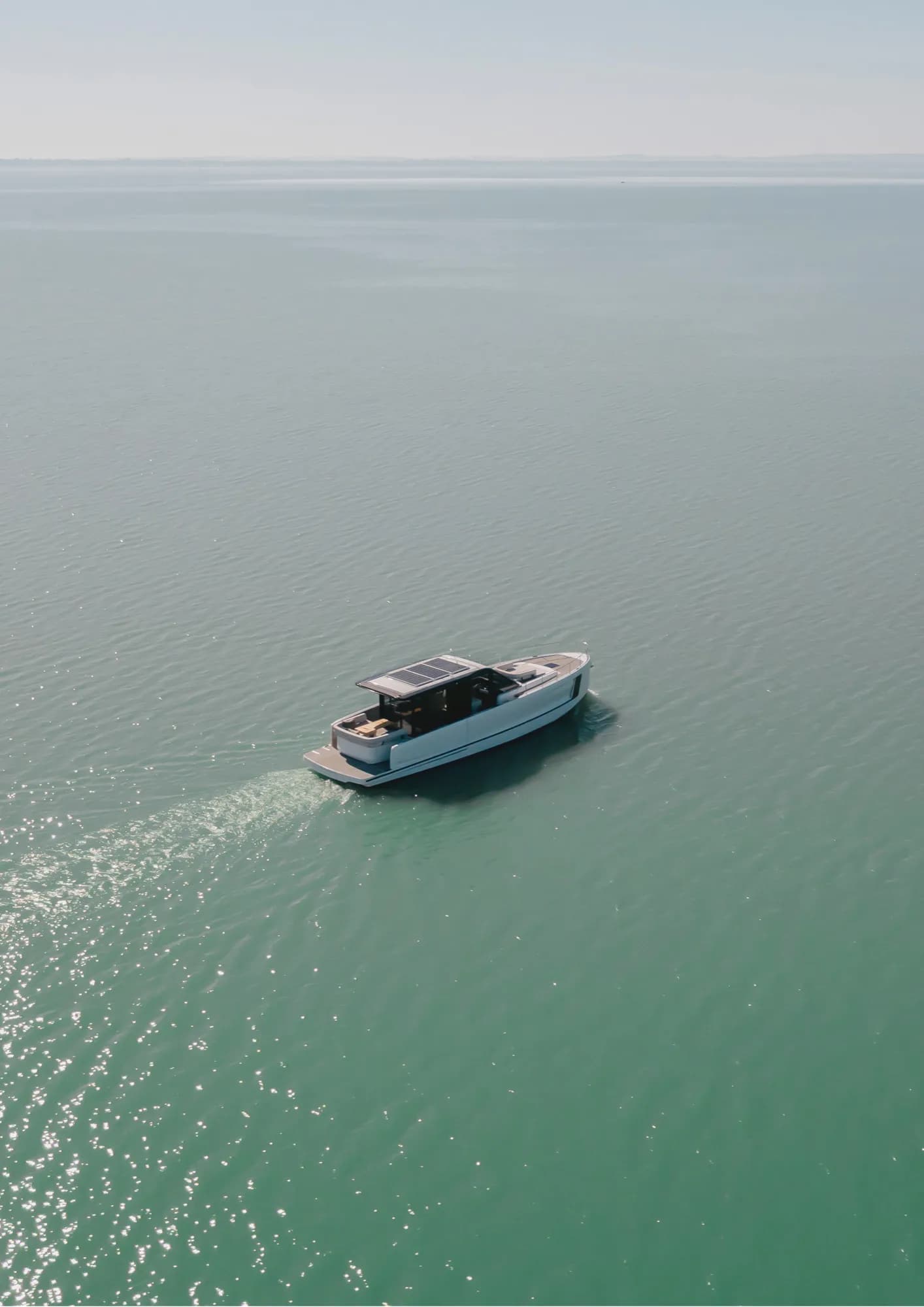 Aerial view of a white Wia yacht cruising alone across calm turquoise open water.