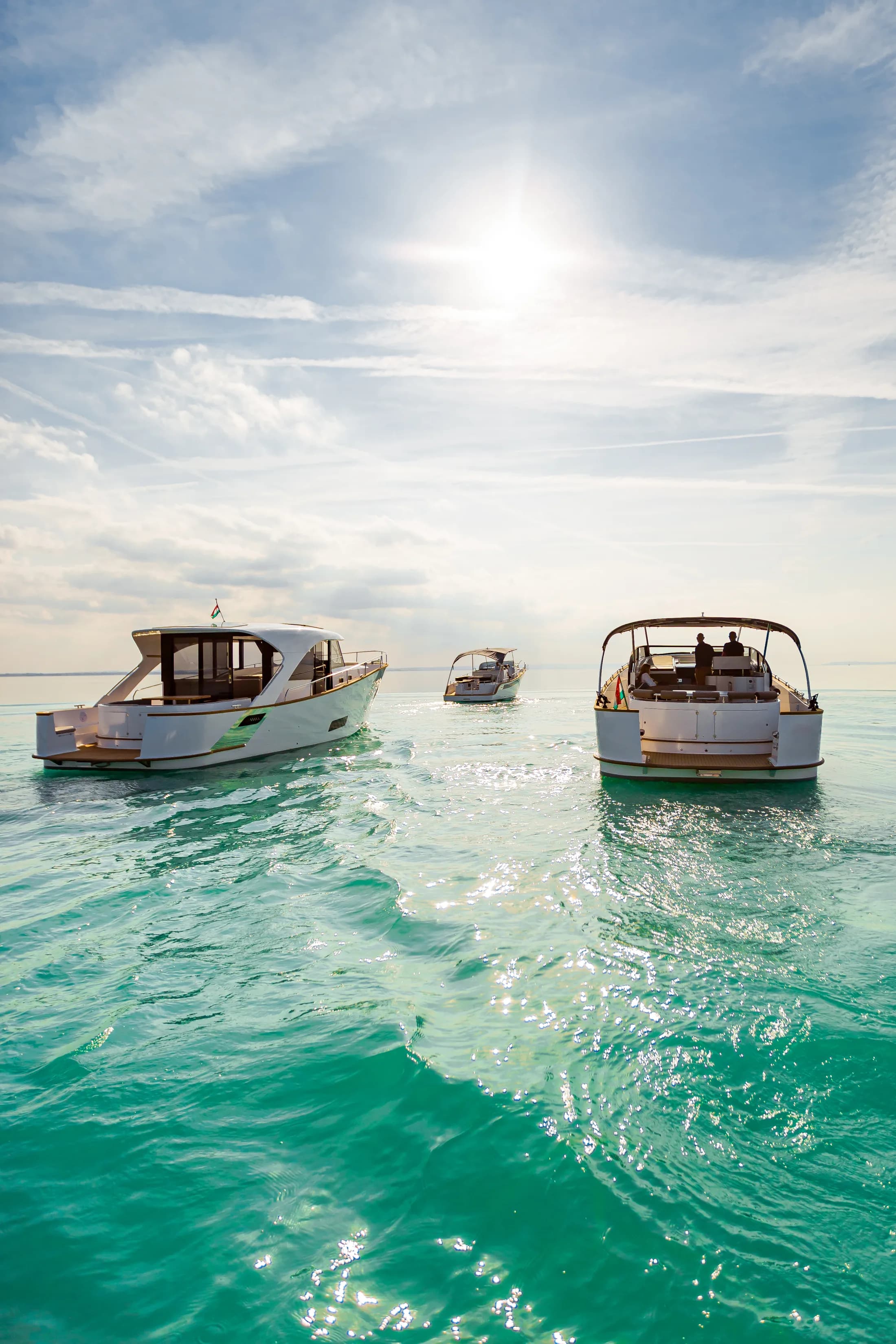 Three white Wia yachts on bright turquoise water under a sunny sky, guests aboard and a Hungarian flag flying.