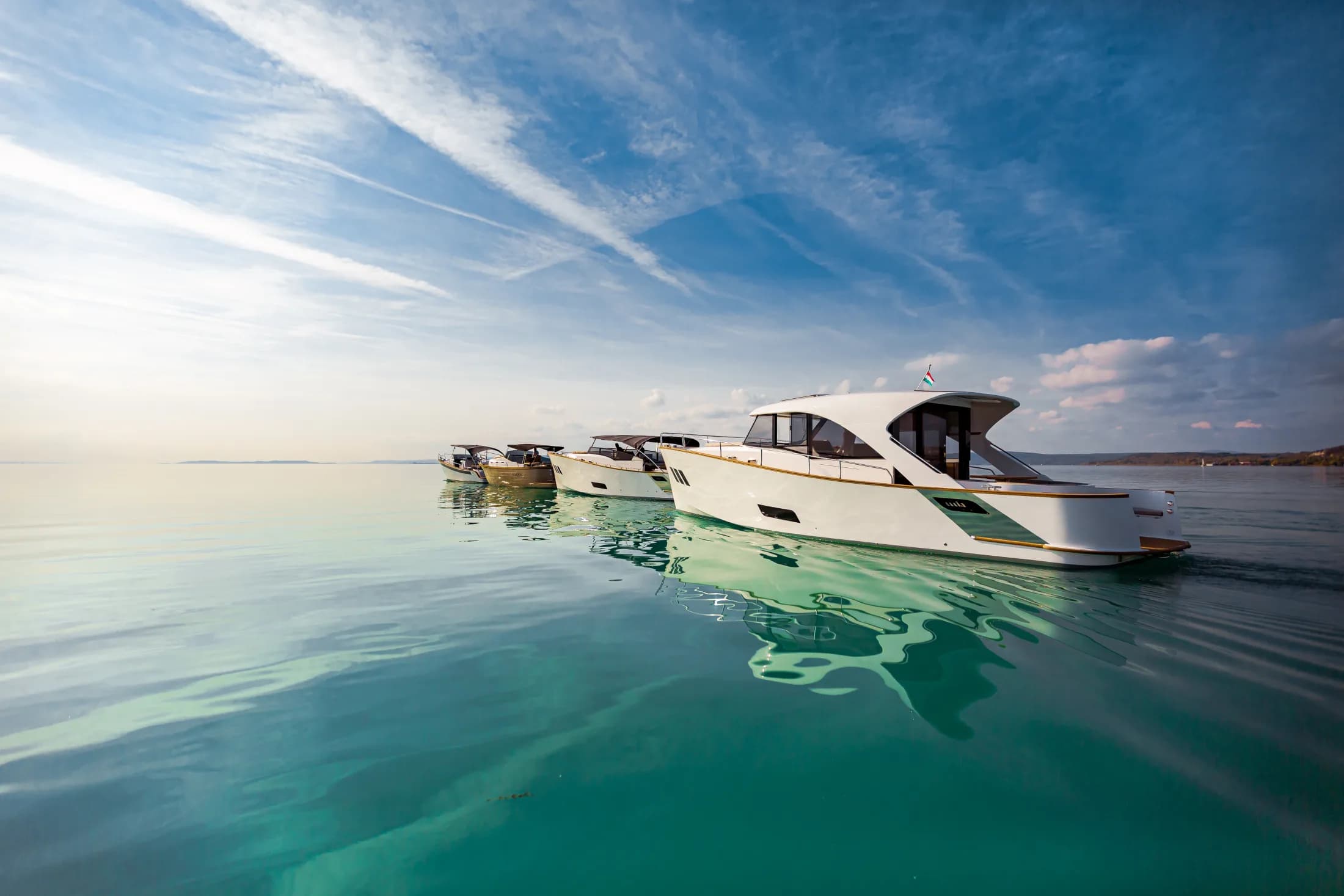A row of Wia yachts on mirror-calm turquoise water at golden hour, their reflections below.