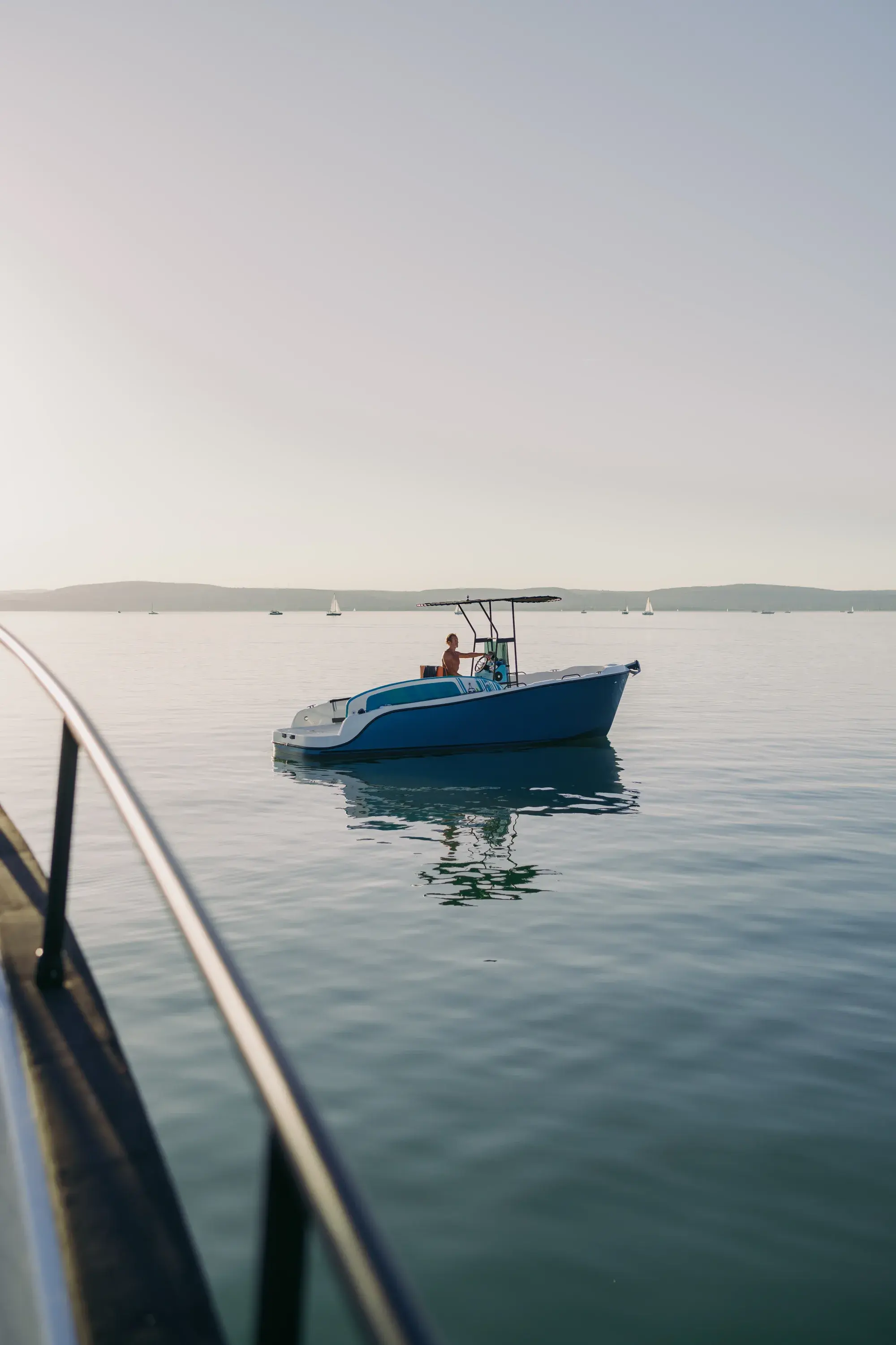 The blue-hulled Wia 230 CC under way, its open deck with orange cushions around the centre console under a black T-top.