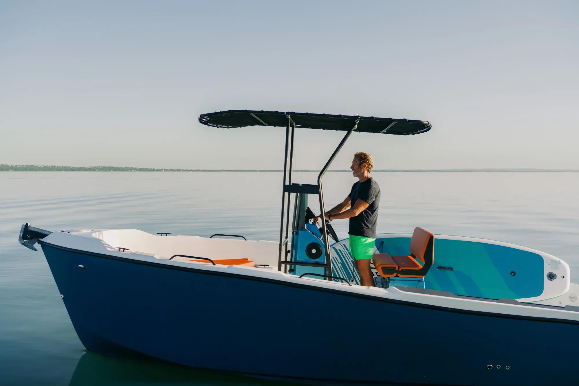The blue-hulled Wia 230 CC under way, its open deck with orange cushions around the centre console under a black T-top.