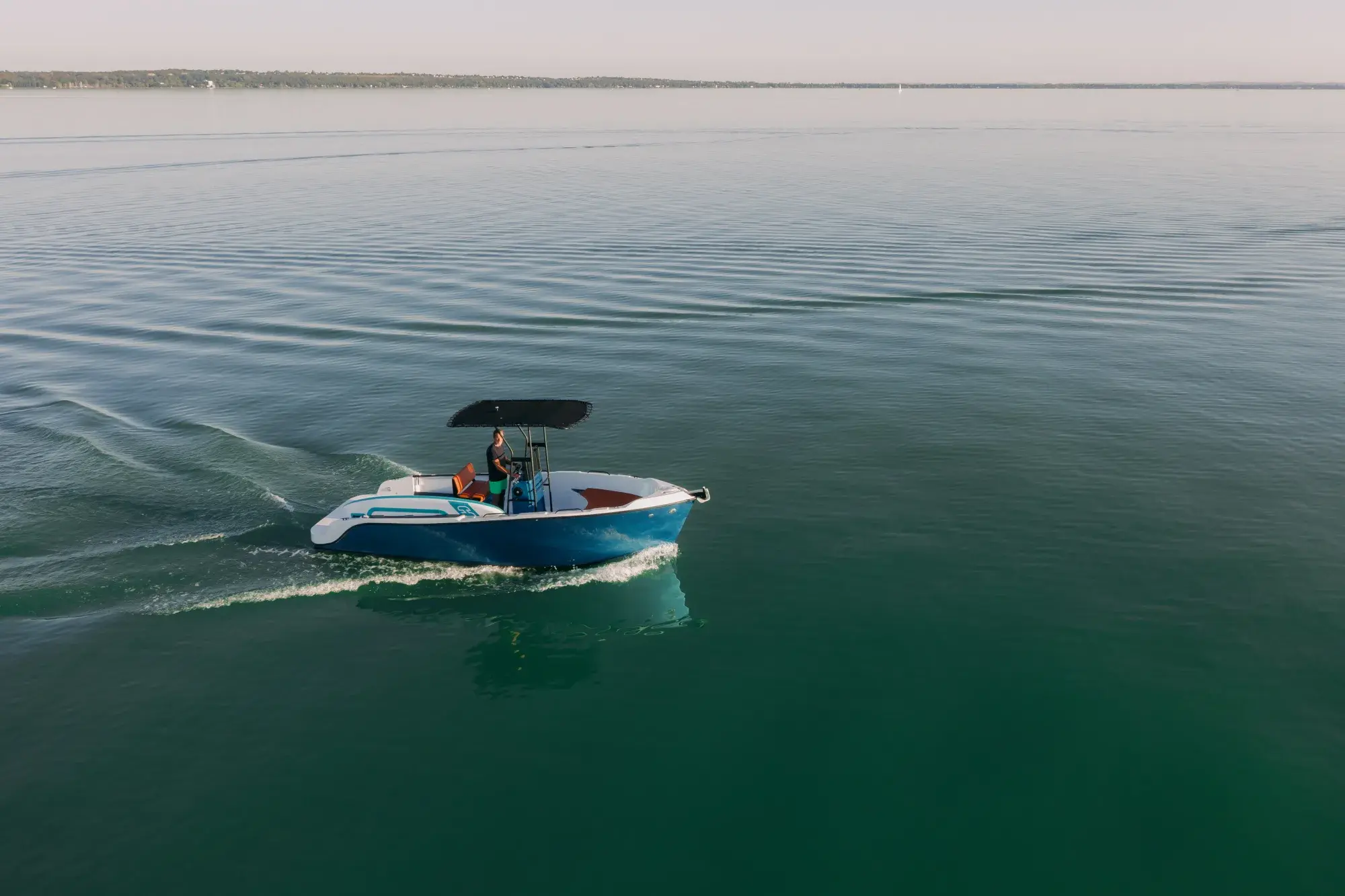 The blue-hulled Wia 230 CC under way, its open deck with orange cushions around the centre console under a black T-top.