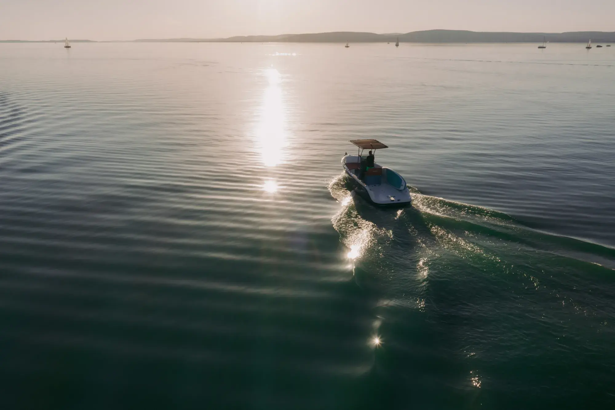 The Wia 230 CC seen from high above, a small open boat with a black T-top leaving a wake across shimmering green water.
