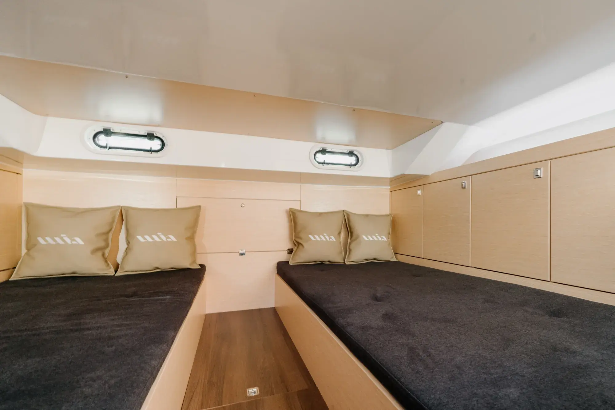 Die Unterdeckskabine des Wia 330: eine U-förmige anthrazitfarbene Sitzgruppe um einen Tisch aus heller Eiche, helle Eichenvertäfelung, eine runde Deckluke und Kissen mit Anker-Motiv.