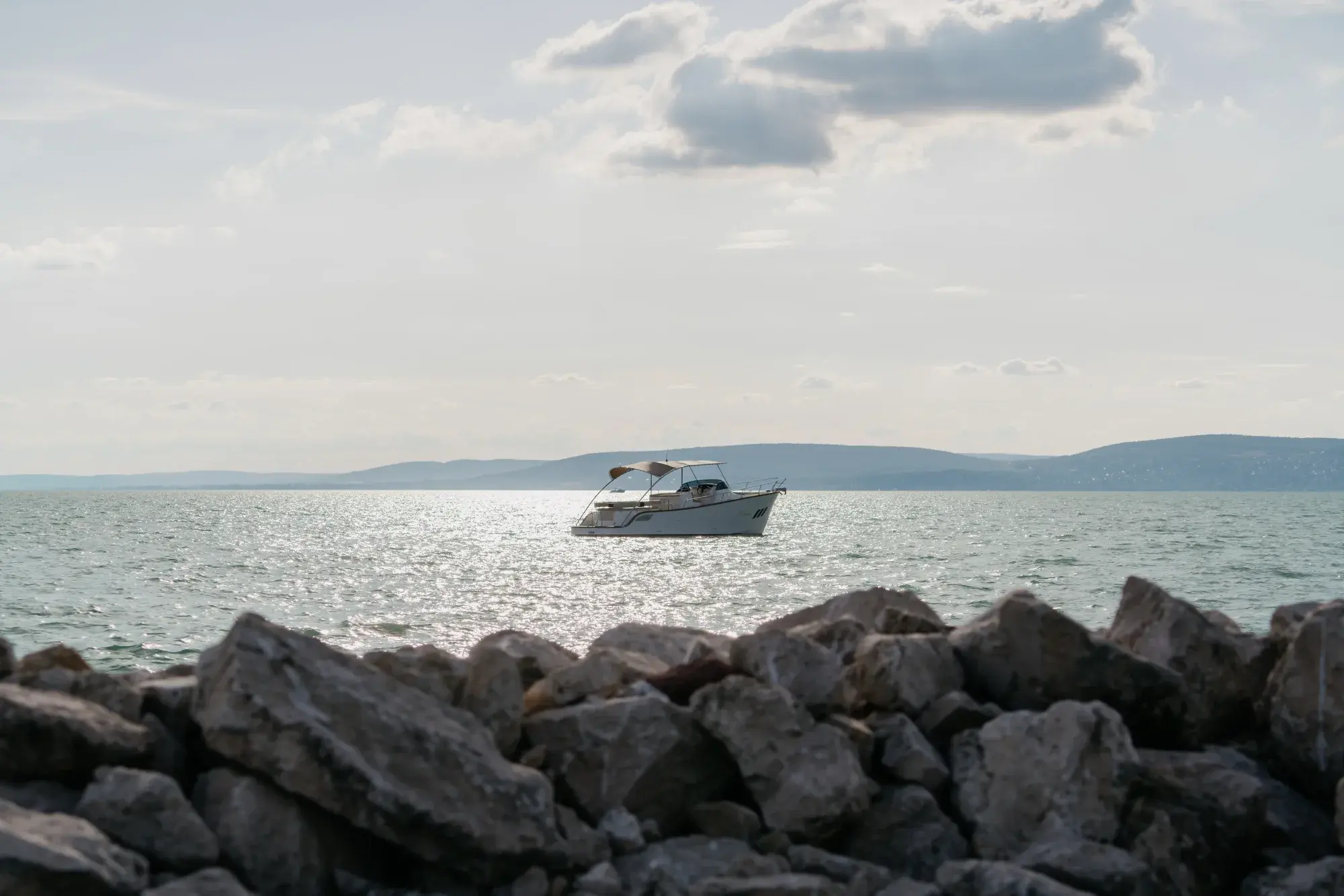 Der Wia 330 aus großer Höhe, ein kleines weißes offenes Boot mit cremefarbenem Verdeck, das eine Kielspur über schimmerndes grünes Wasser zieht.