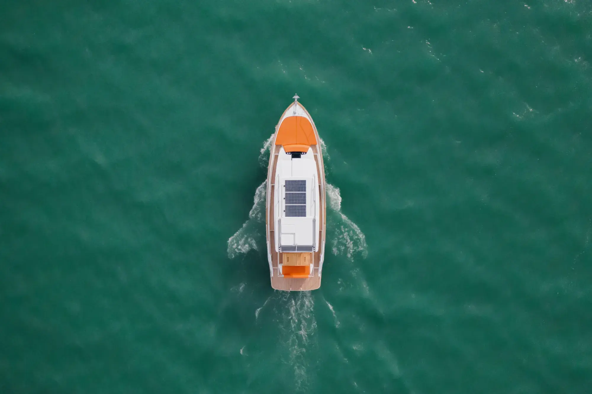 Der Wia 350 senkrecht von oben, sein weißes Hardtop, die Teak-Seitendecks und orangefarbene Sonnenliegen auf grünem Wasser.