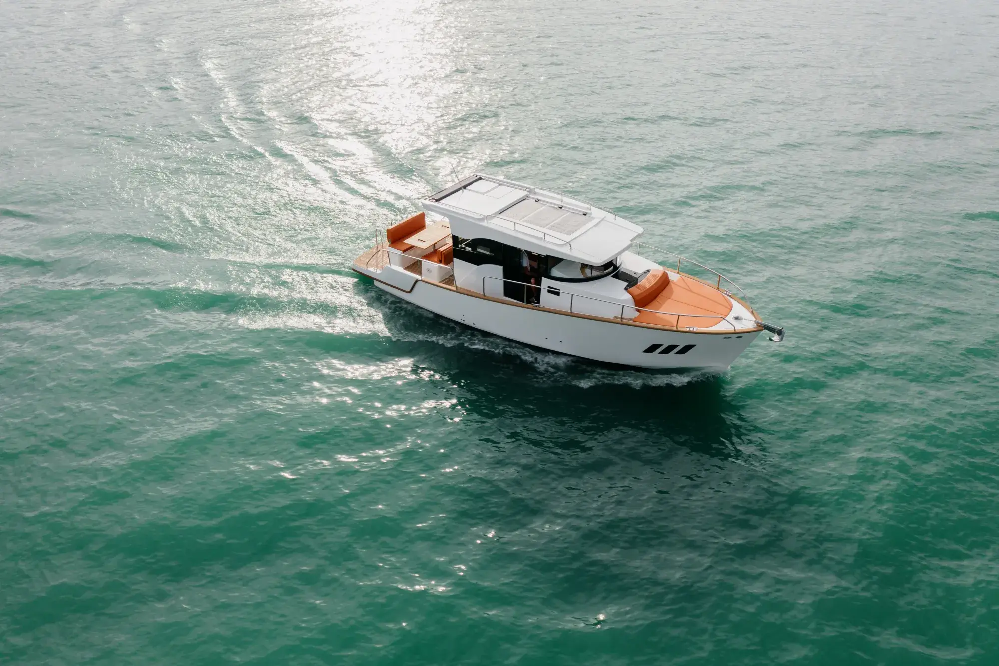 Der Wia 350 Hardtop-Cruiser mit weißem Rumpf und orangefarbener Polsterung in Fahrt auf türkisfarbenem Wasser, aus der Luft.