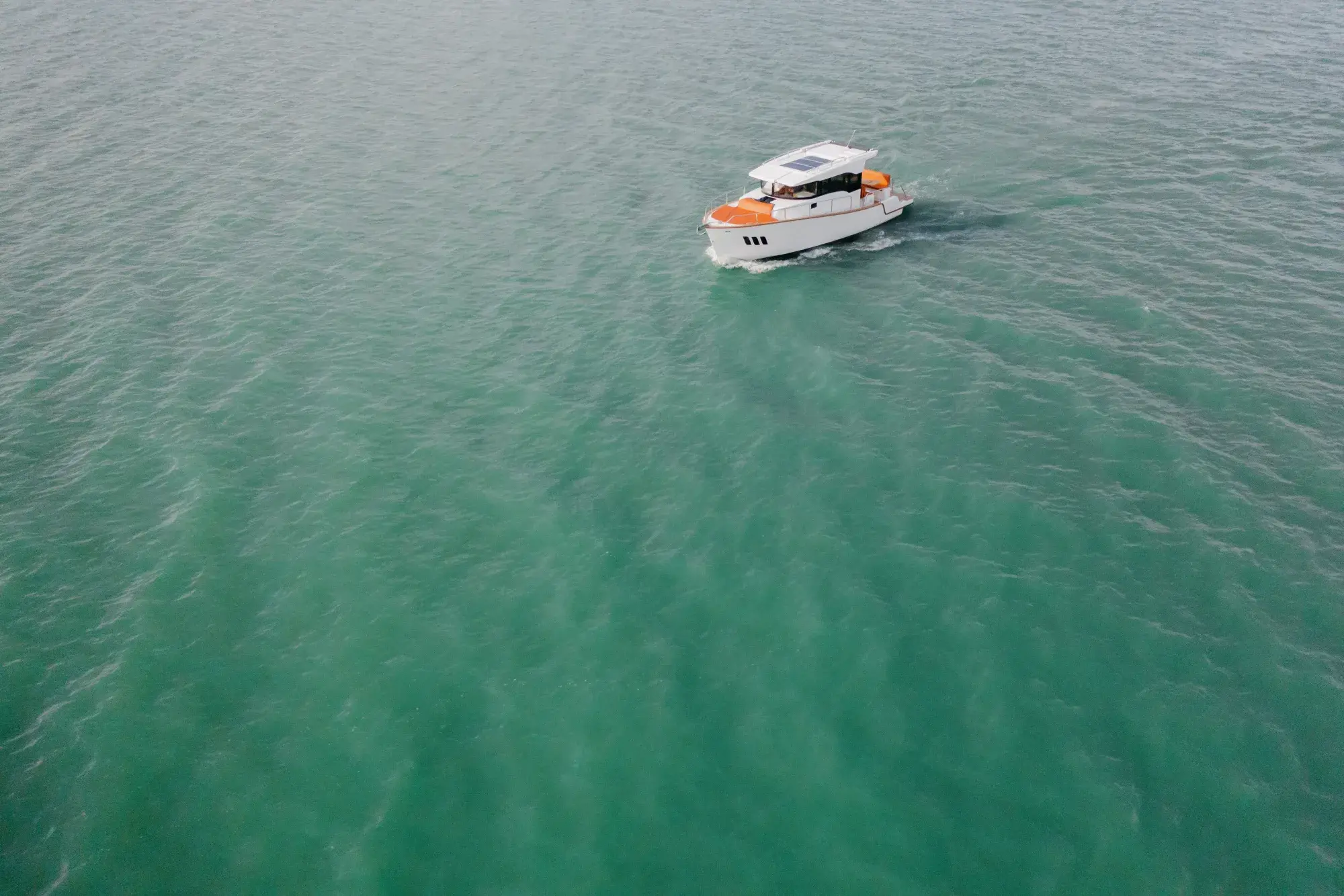 Der Wia 350 aus großer Höhe, ein weißer Hardtop-Cruiser, der eine Kielspur über schimmerndes grünes Wasser zieht.